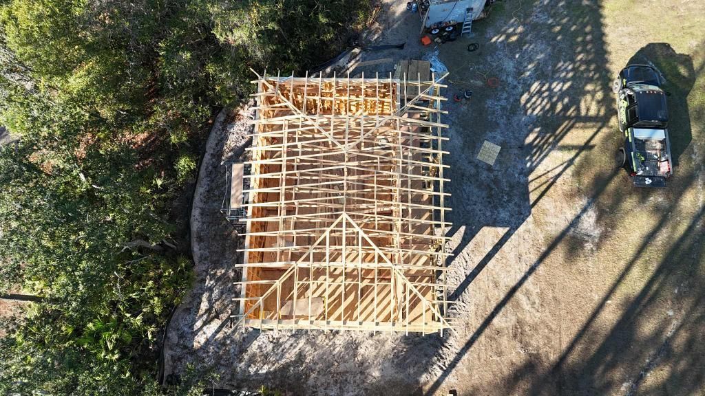 Framed wooden structure for a building with trusses and rafters in a sunny outdoor setting.