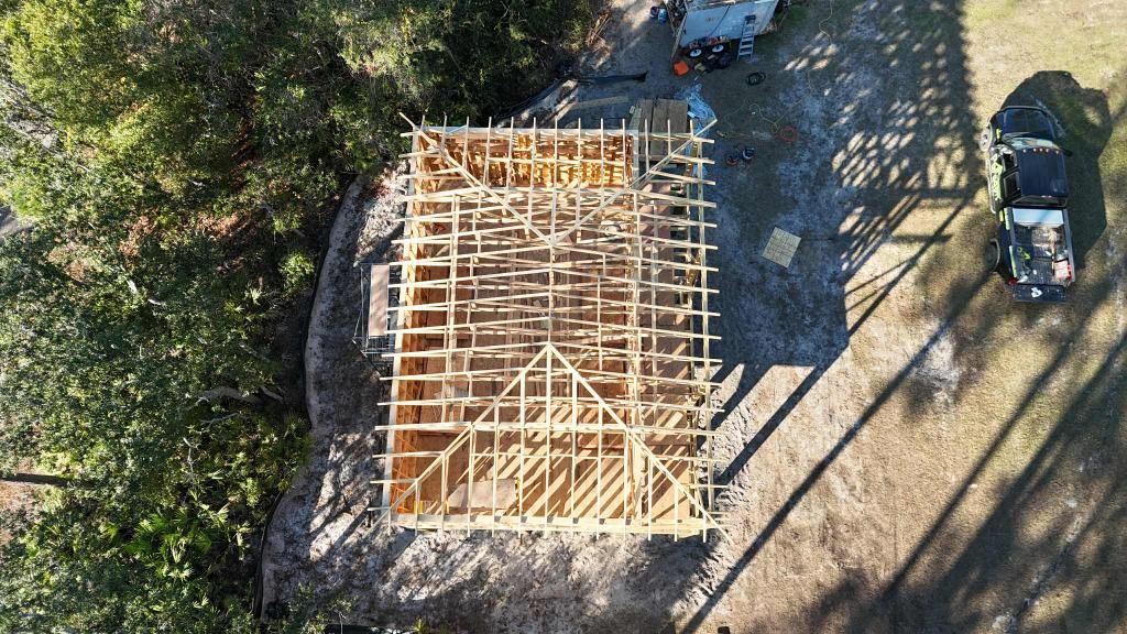 Light blue beach house on stilts with deck being built, construction materials, gravel, and sandy beach.