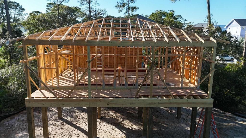 Wooden structure of a building under construction, raised on posts, roof framework visible.