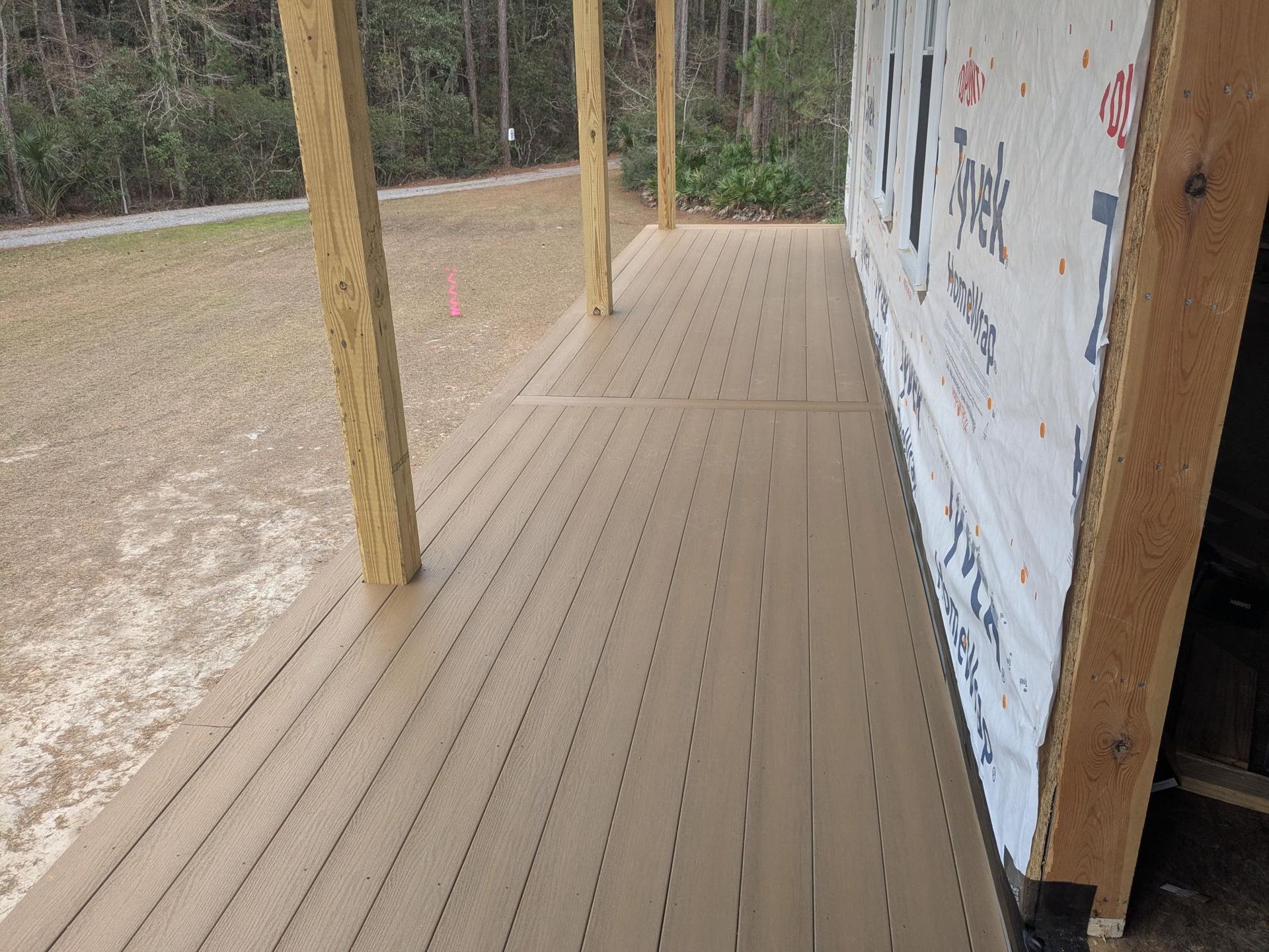 A partially-built outdoor deck with composite decking and support posts. The house is wrapped in moisture barrier.