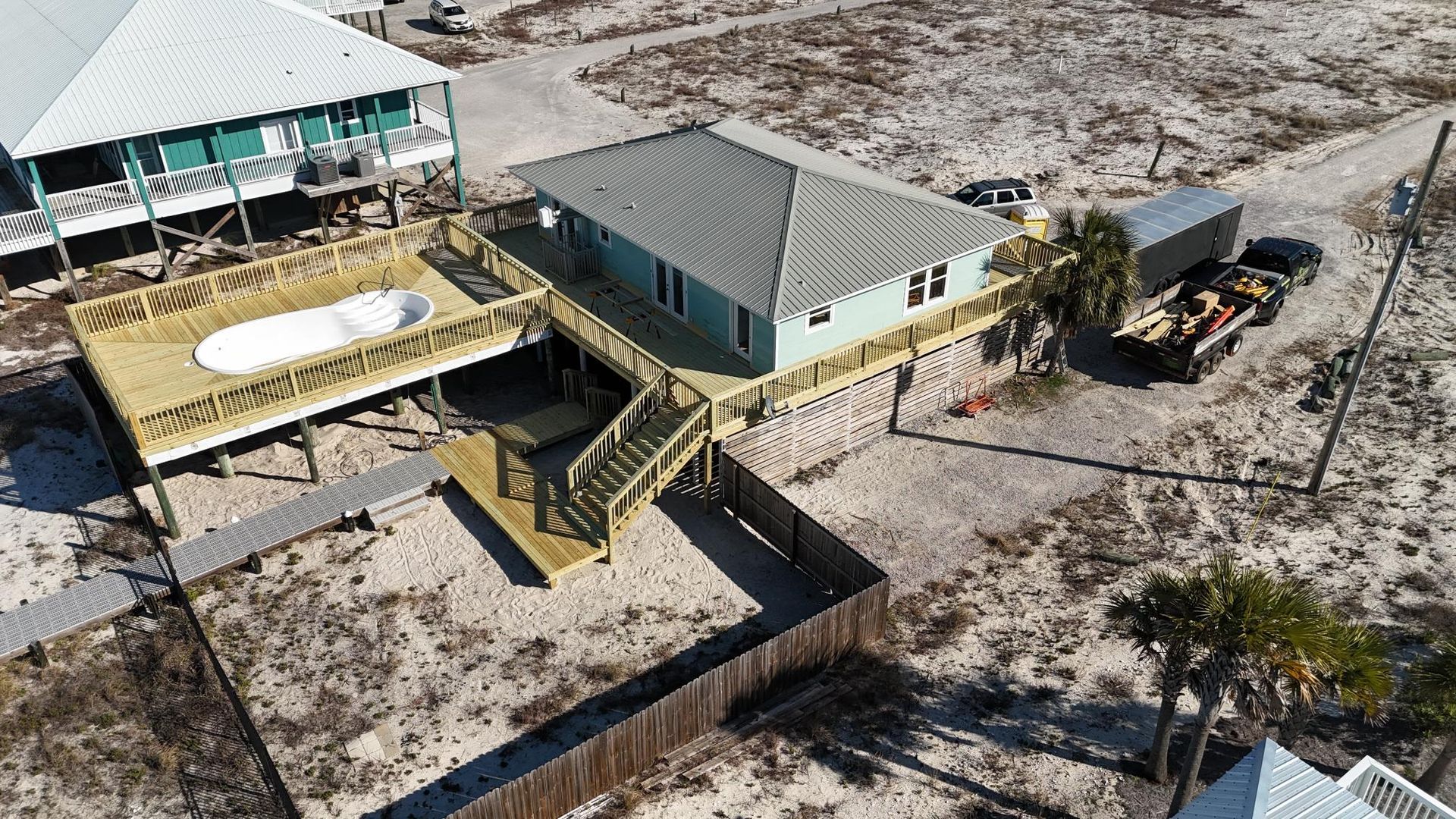Elevated house with gray roof, large deck, and small pool on a sandy lot.