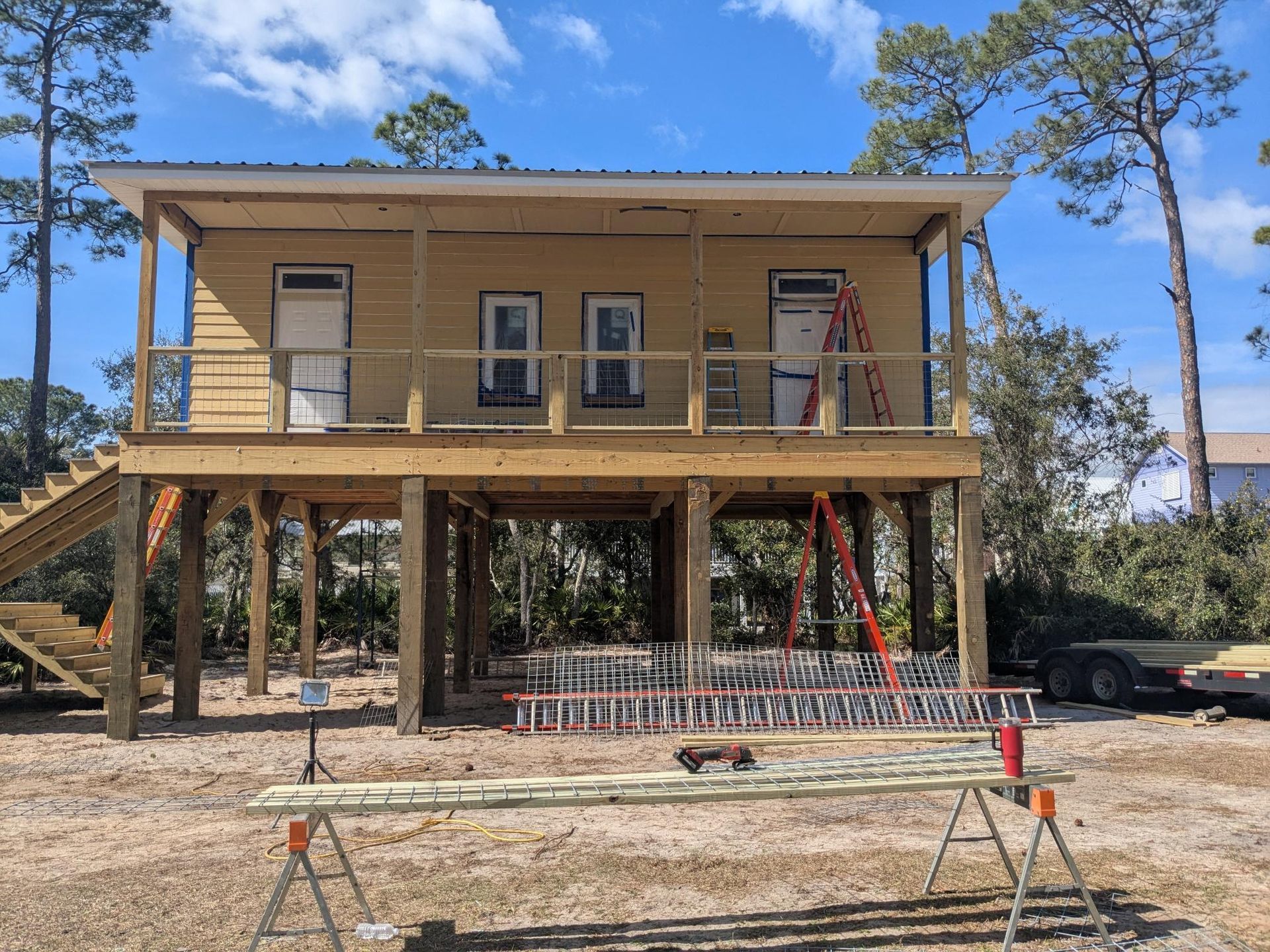 Two-story house under construction on stilts, with stairs to upper level, yellow siding, and many ladders.