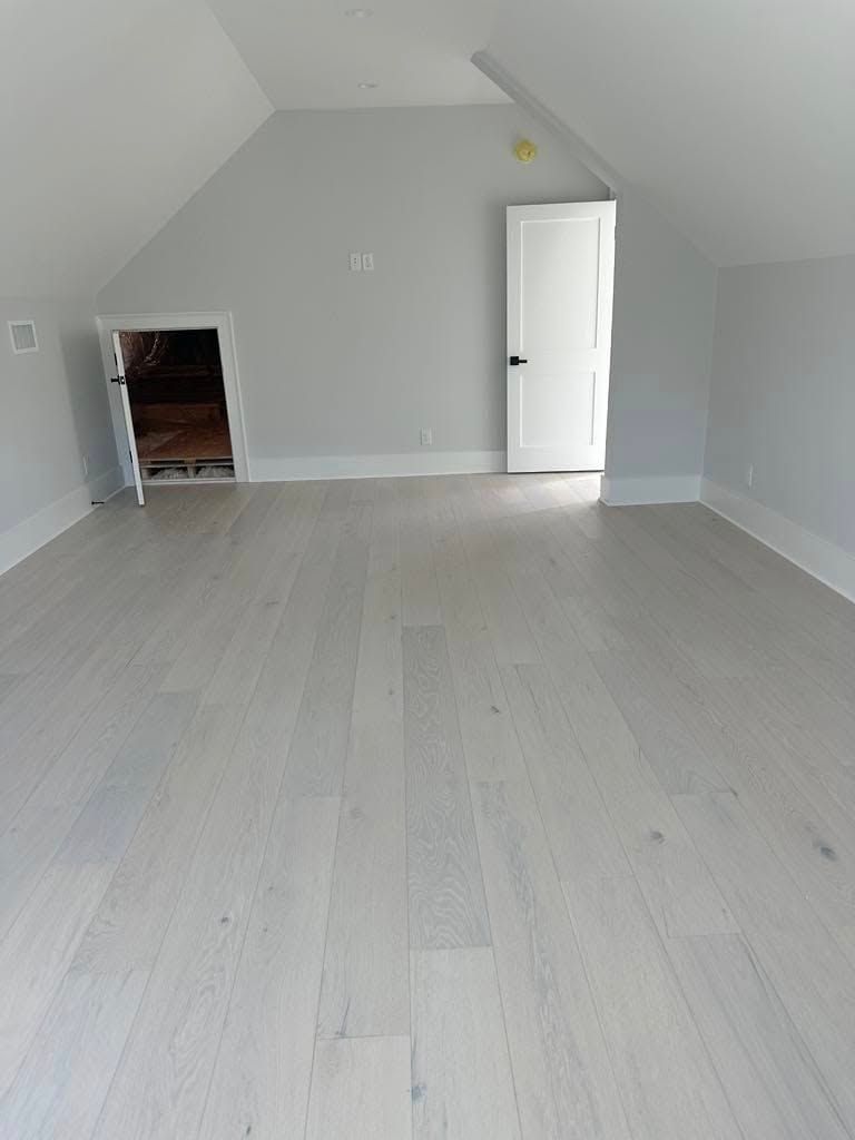 Empty attic room with light wood floors, white walls, and a storage door.