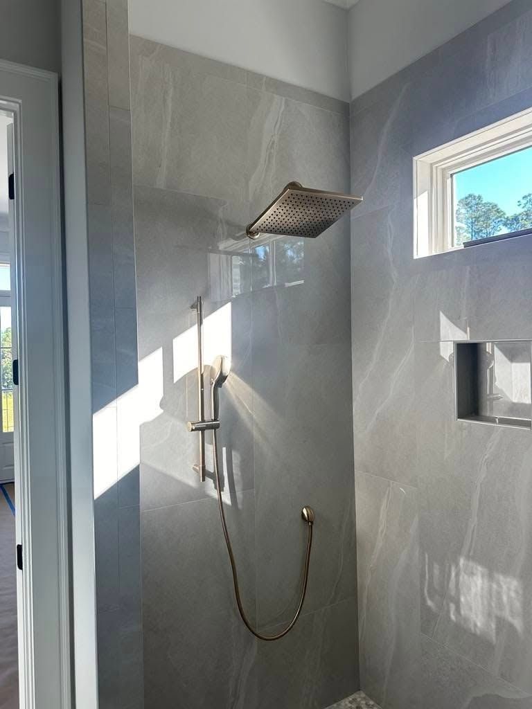 Shower with gray tiled walls, rain showerhead, hand shower, and a small window.