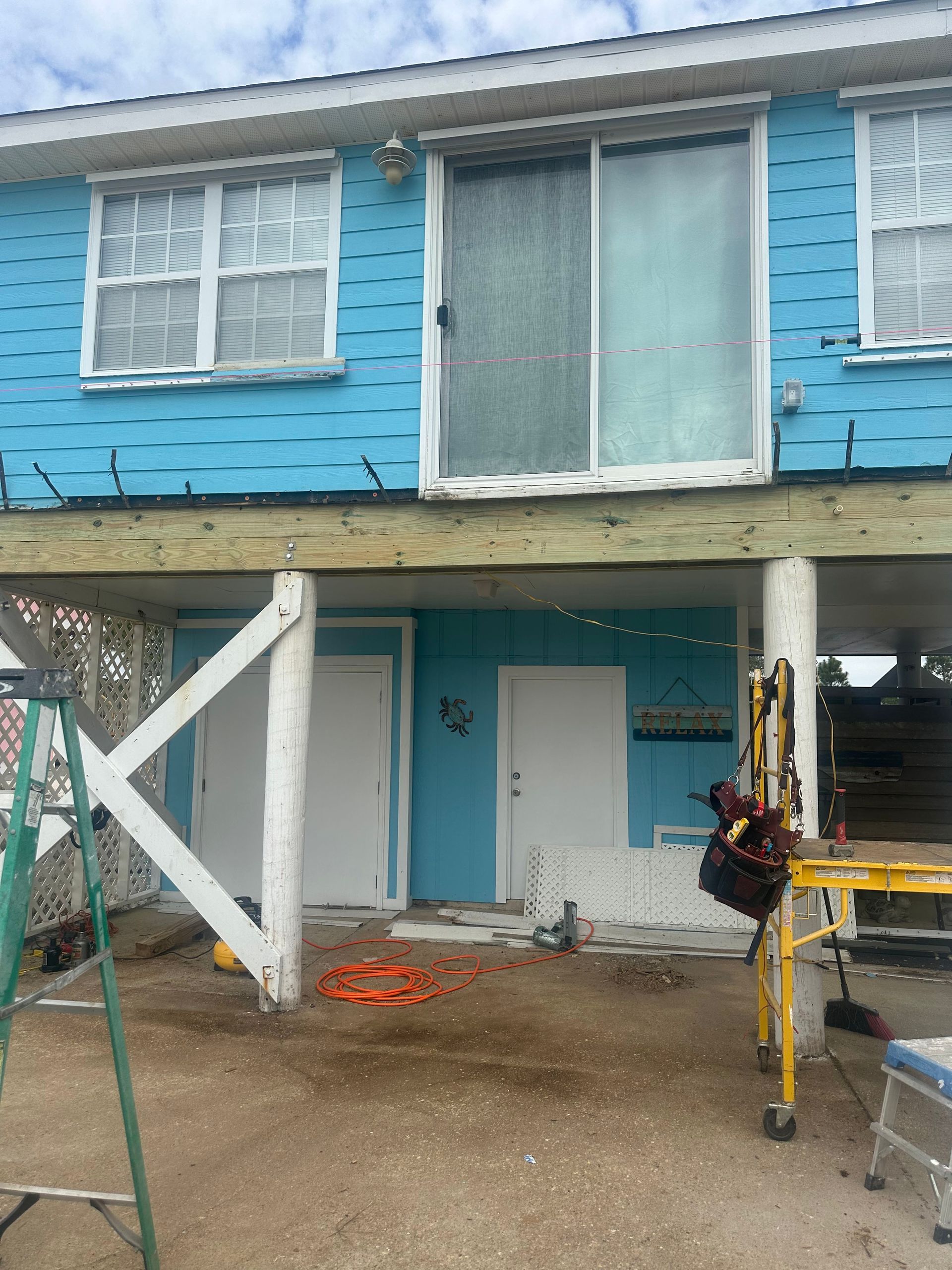 Blue house on stilts under construction, with doors and a sliding glass door.
