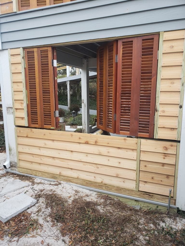 Exterior view of a window with brown shutters, surrounded by unfinished wooden siding.