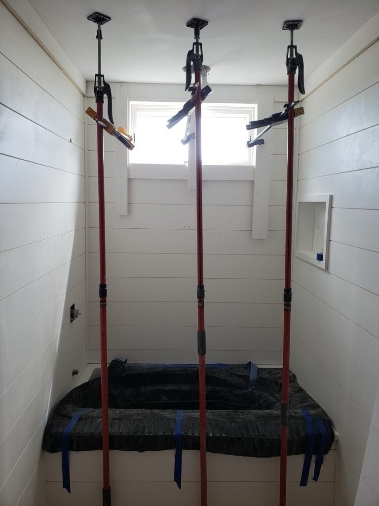 Three adjustable support poles in a small room, holding up a ceiling above a covered surface.