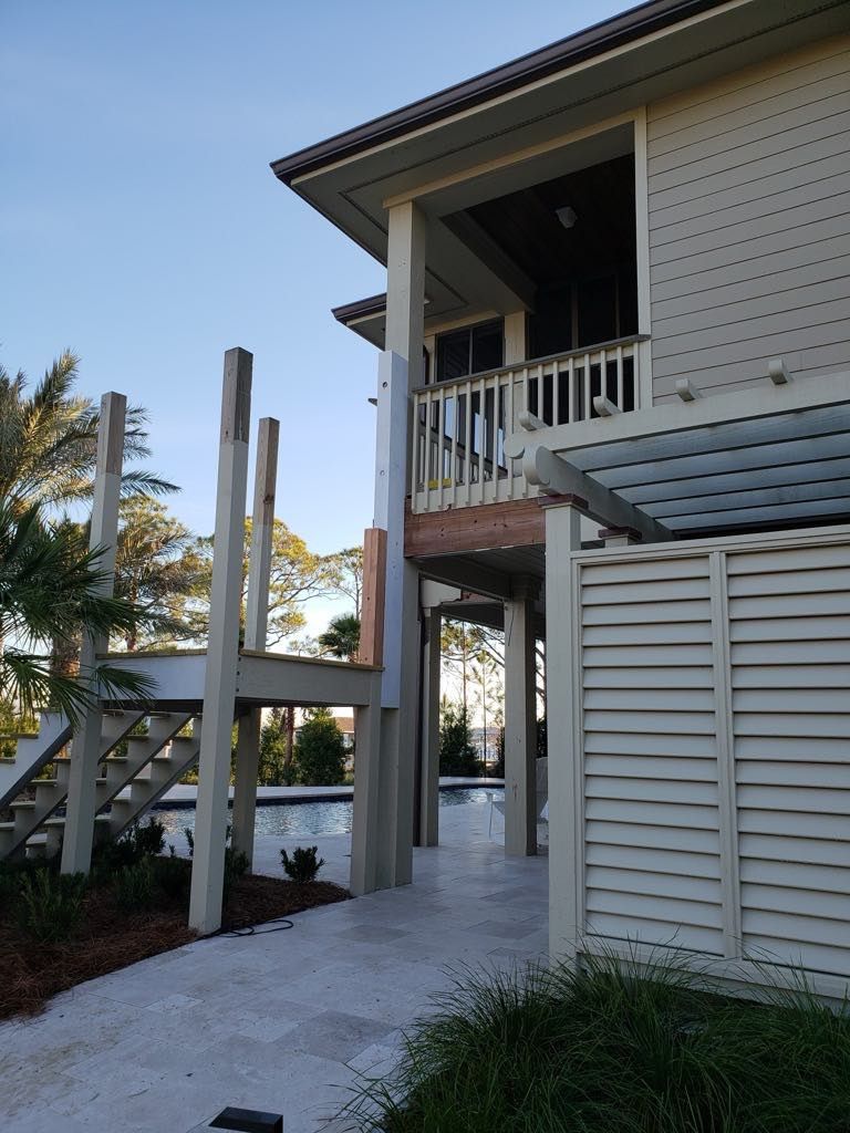 Exterior of a light-colored house with a deck, stairs, and a pool in the background.