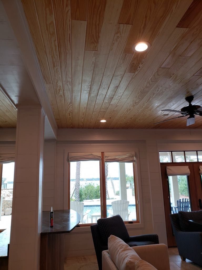 Wood plank ceiling with recessed lights, above a room with windows and furniture.