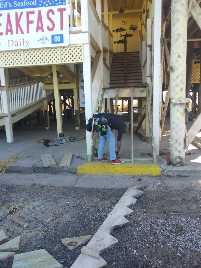 Person working on a ramp at Ed's Seafood restaurant. Yellow caution strip, stairs in background, weathered wooden structure.