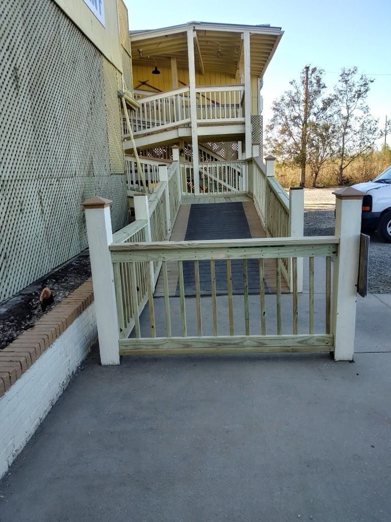 Wooden ramp leading up to a two-story building. Light green wooden railings and gray concrete.