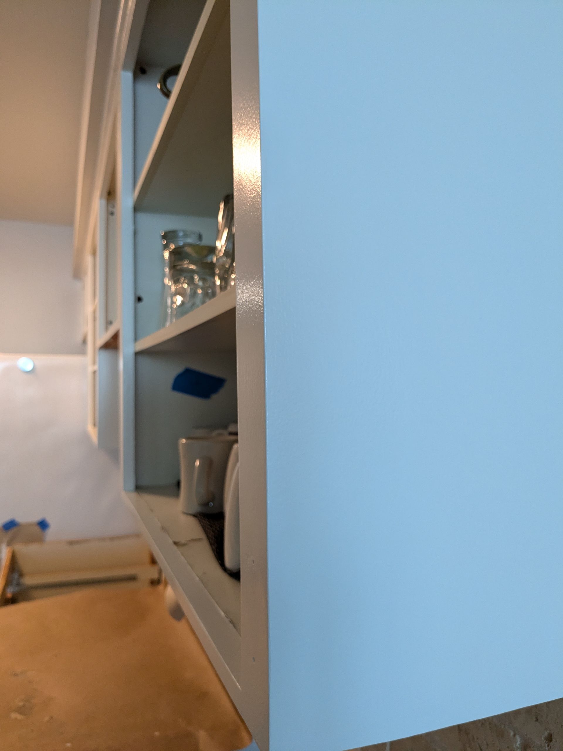 White kitchen cabinet with open shelves, displaying items. Blue wall.