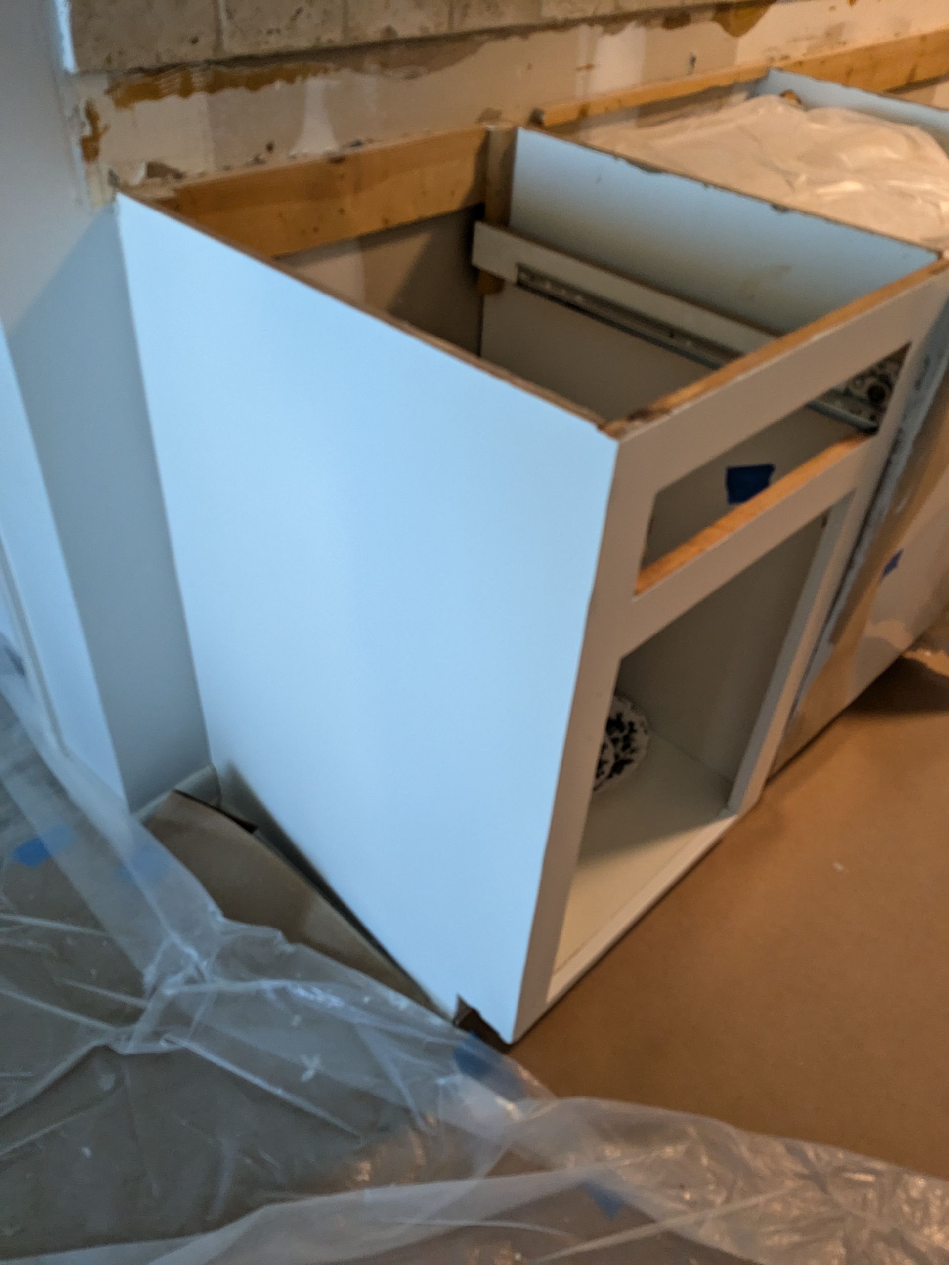 White kitchen cabinet with exposed frame, angled and unfinished, under construction.