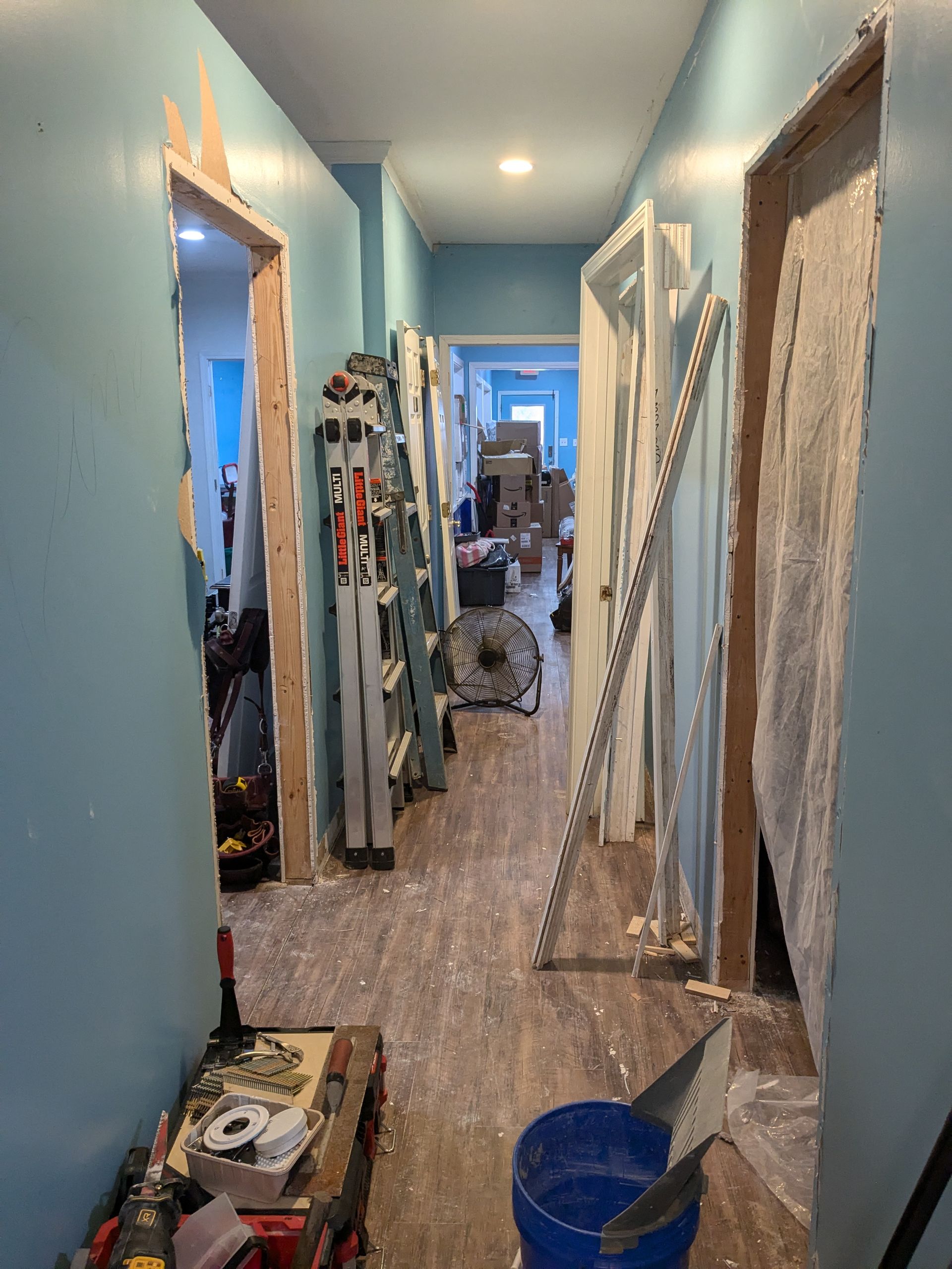 Hallway under renovation with blue walls, open doorways, and construction materials.
