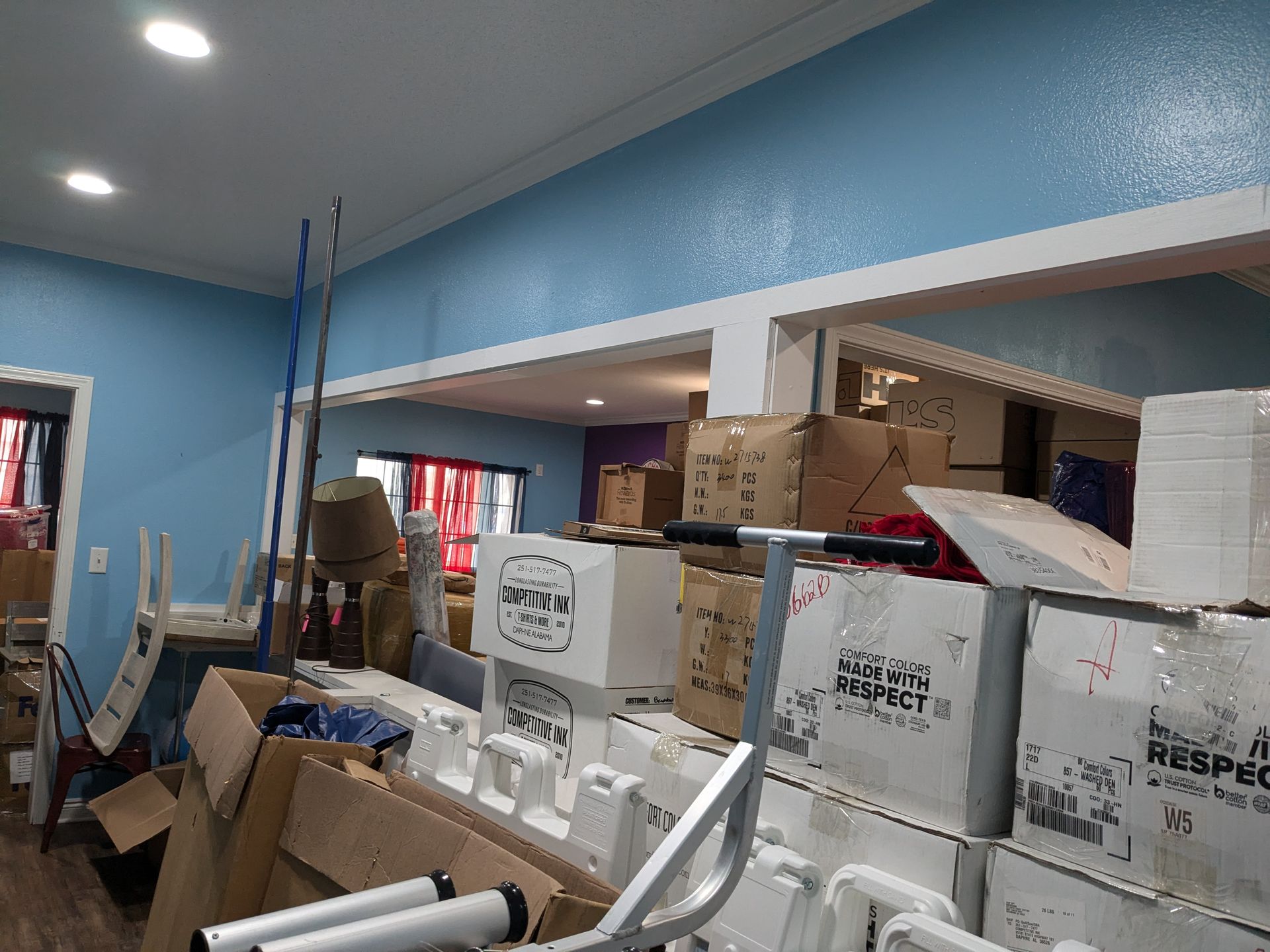 Interior of a cluttered room with blue walls, boxes, and miscellaneous items; an opening to another room is visible.