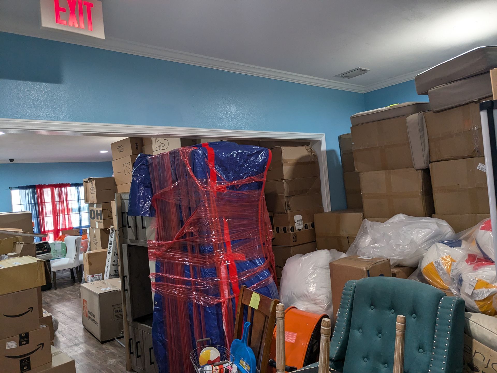 Interior packed with boxes and furniture; Exit sign above doorway.