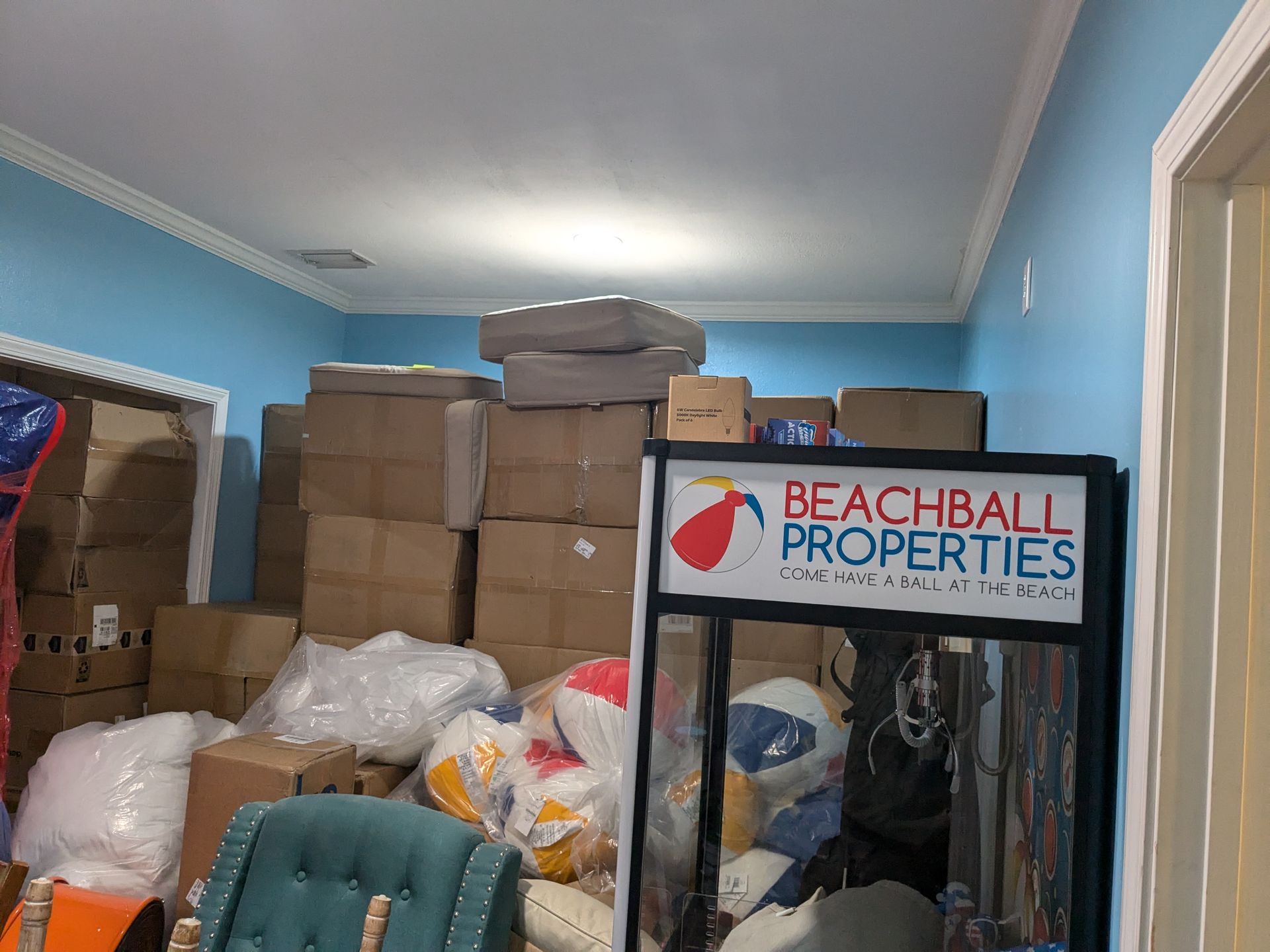 Room filled with stacks of cardboard boxes and various items. Sign for 
