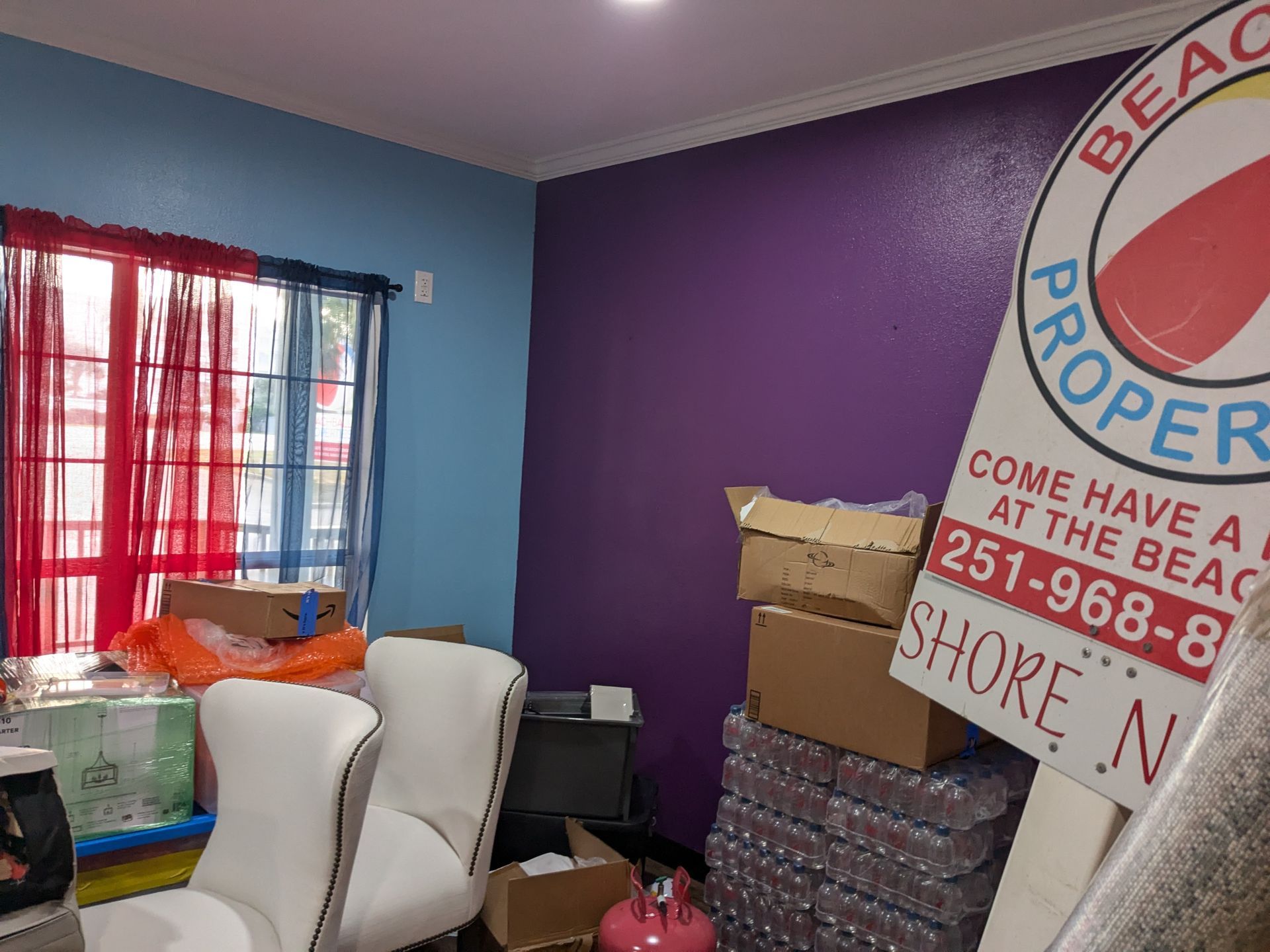 Room with blue and purple walls, red-curtained window, office supplies, and a 