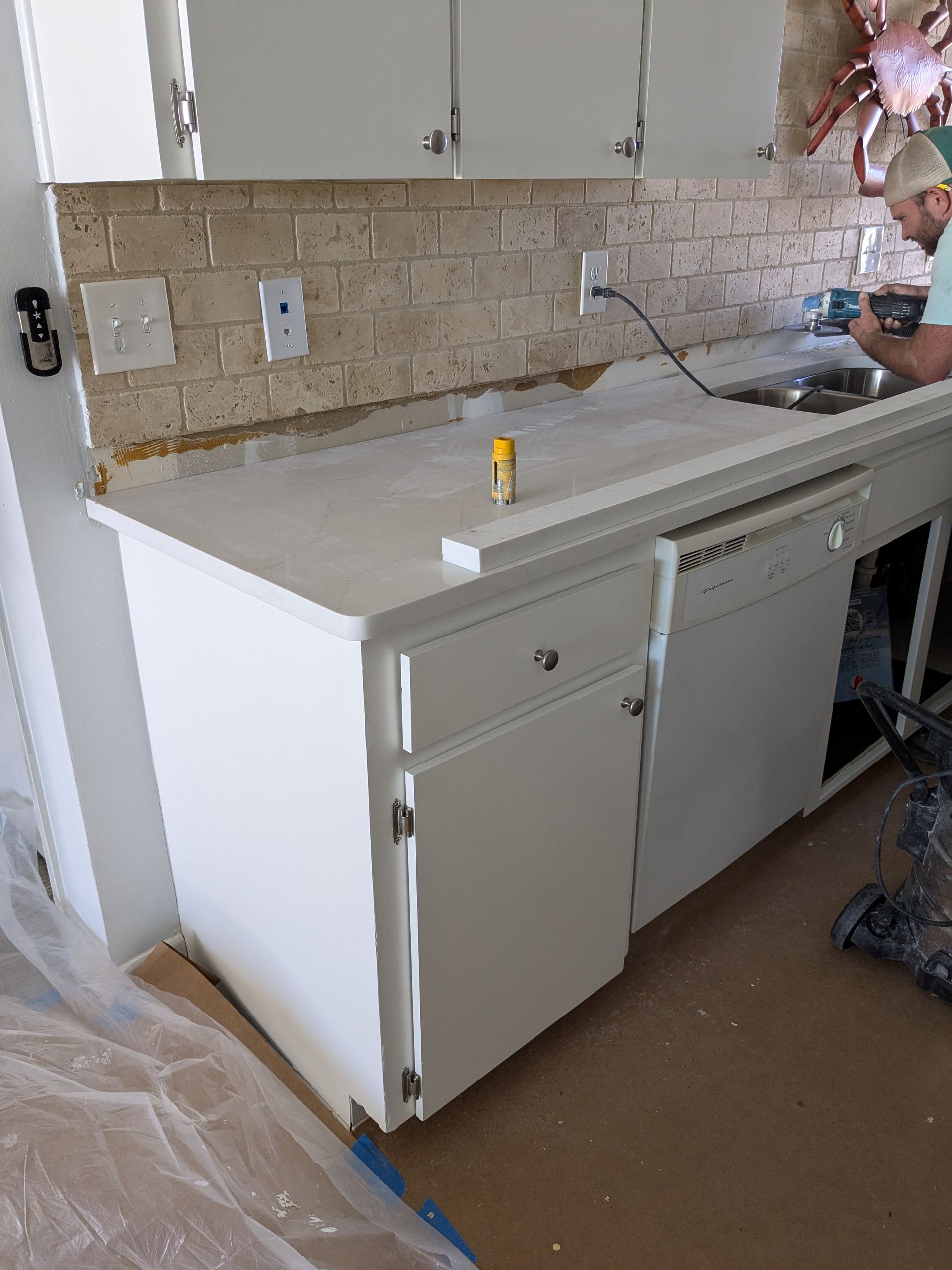 White kitchen cabinets with white countertop and tile backsplash; person working.