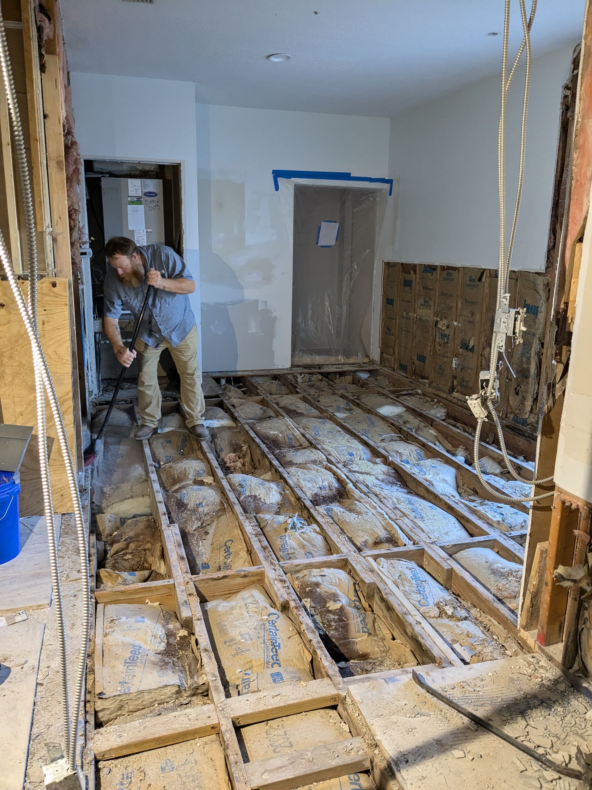 Man demolishing a floor in a room under renovation. Exposed floorboards, bare walls, and a doorway.