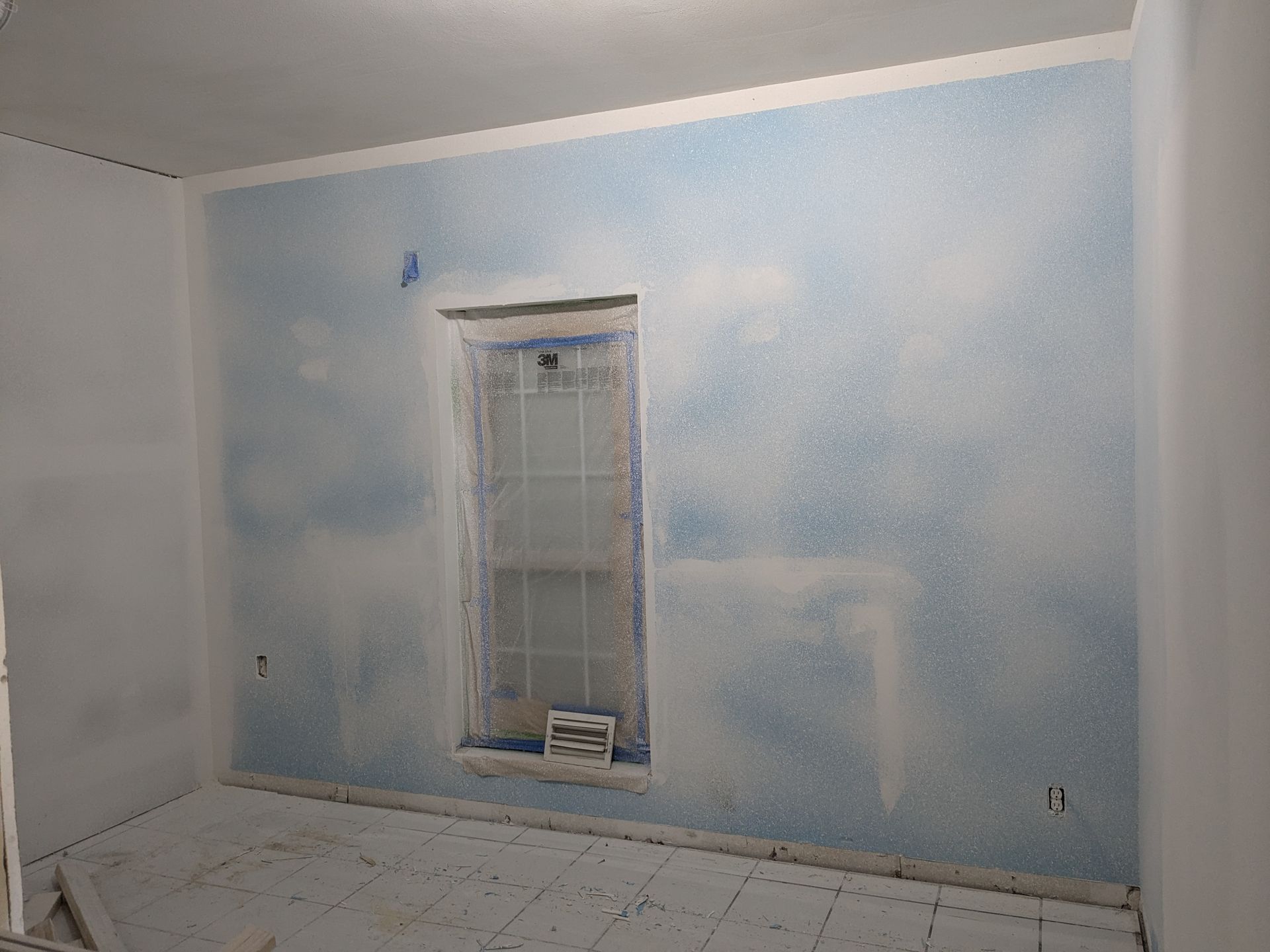 Room with a blue, cloud-like painted accent wall and a window, white trim and ceiling. Unfinished floor.