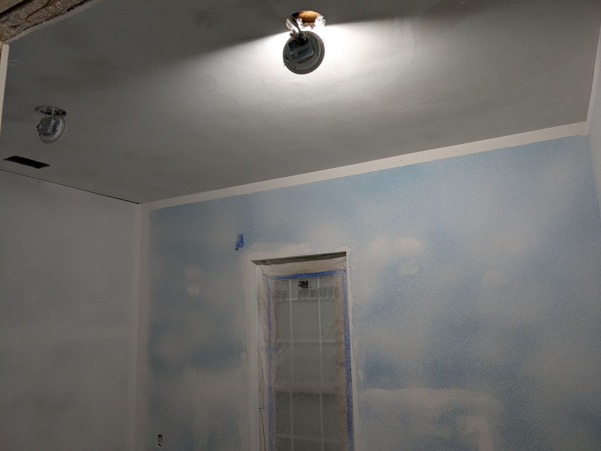Interior room with light blue wall, window, ceiling light, and ventilation.