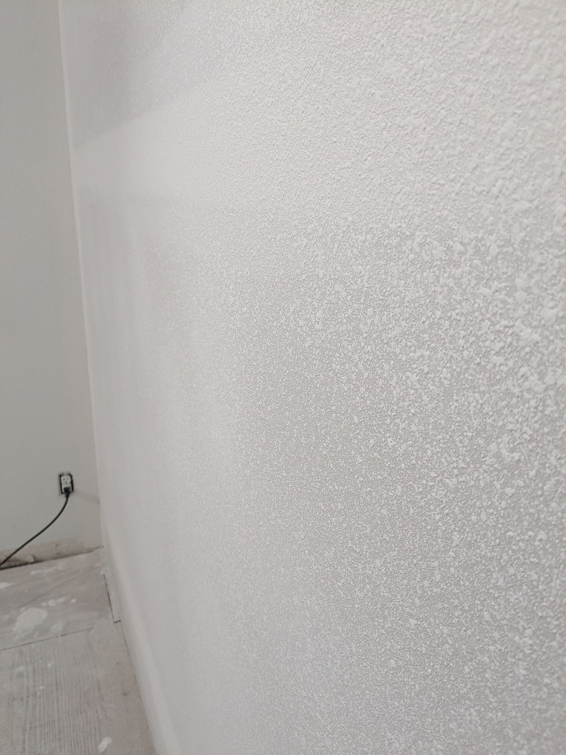 White textured wall, with an electrical outlet and cord on the left.