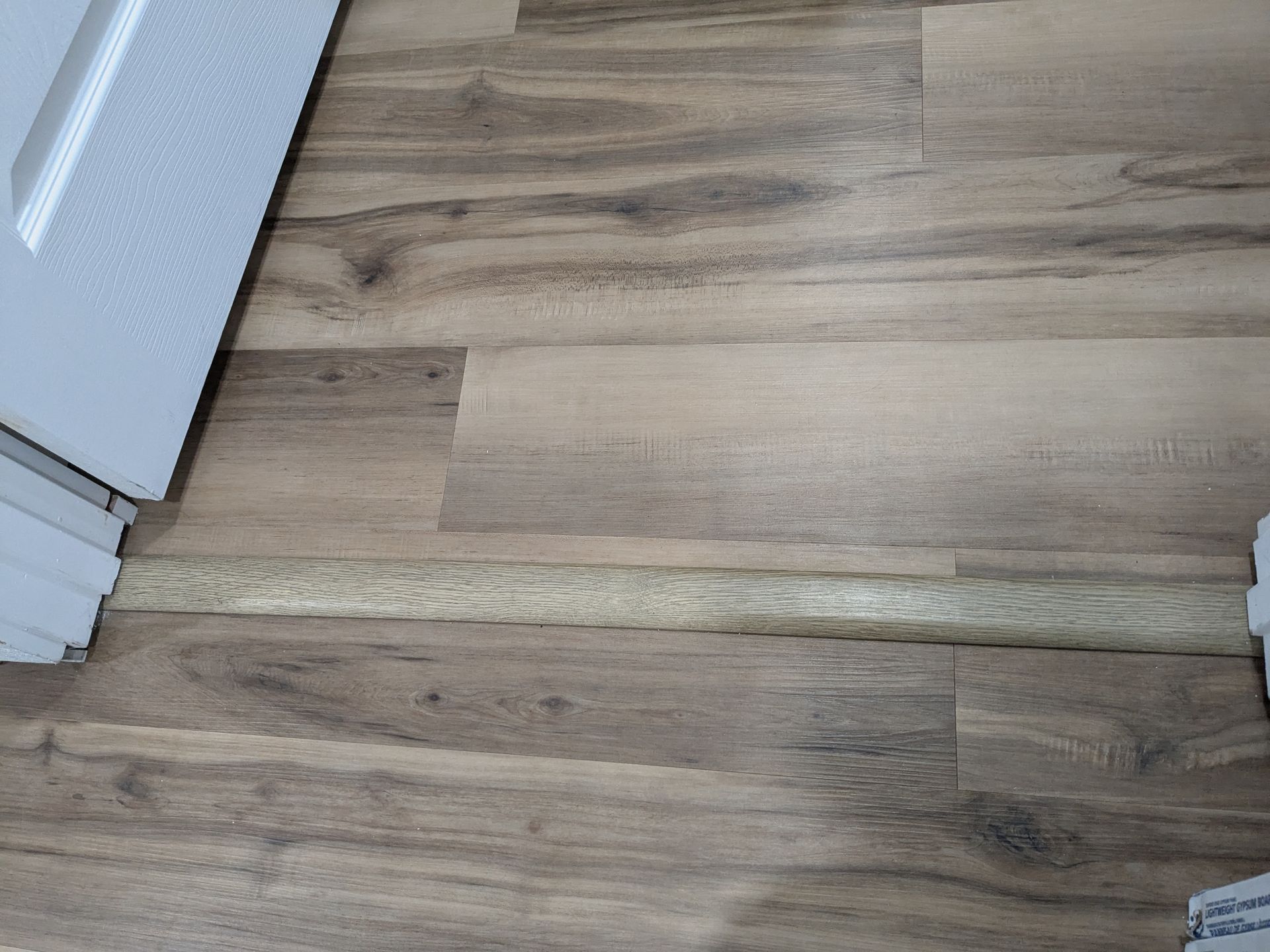 Wooden floor with a light-colored transition strip between rooms, near a white door frame.