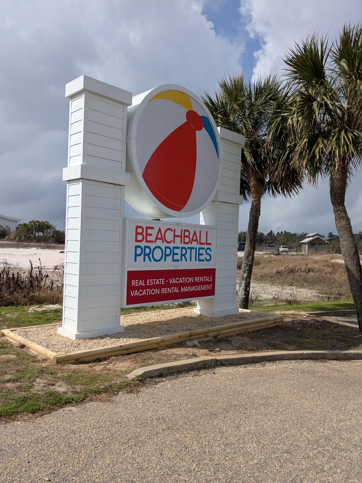 Sign for Beachball Properties: white, beach ball logo, text, palm trees, blue sky.