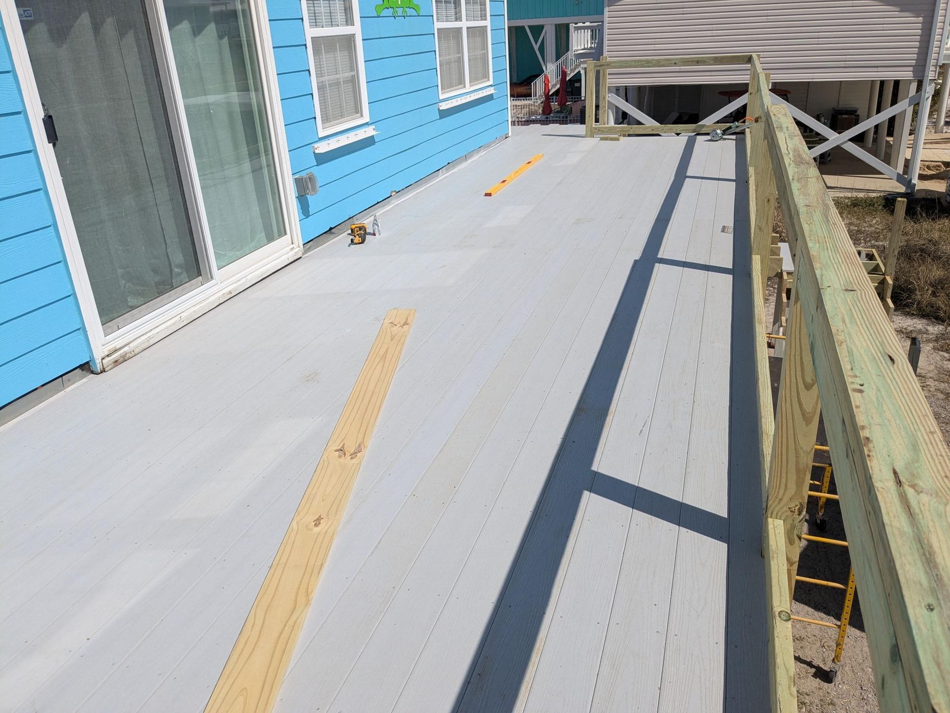 Gray deck with wooden railing and blue house; construction in progress.