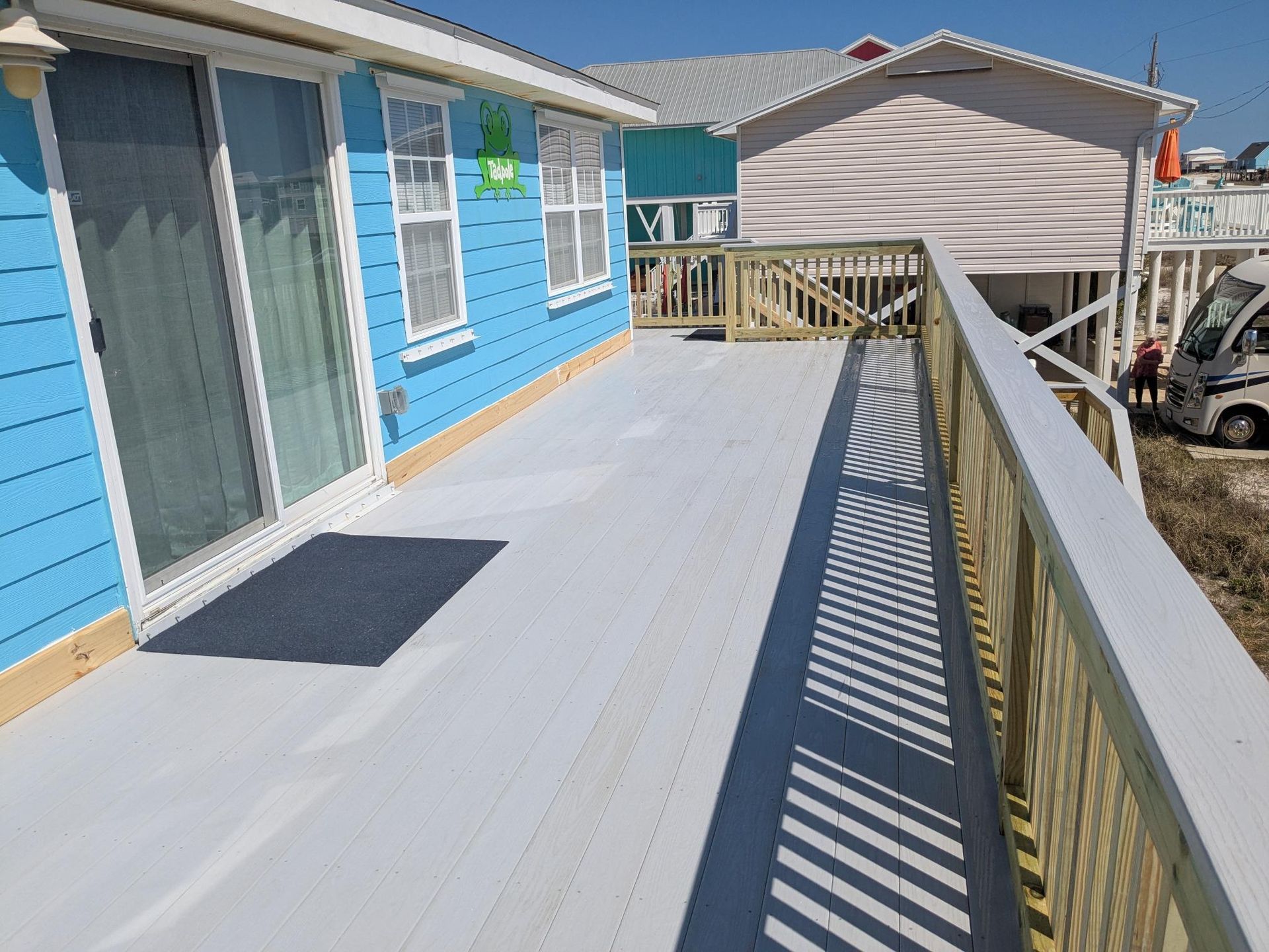 Blue beach house with a white deck and wooden railing on a sunny day.