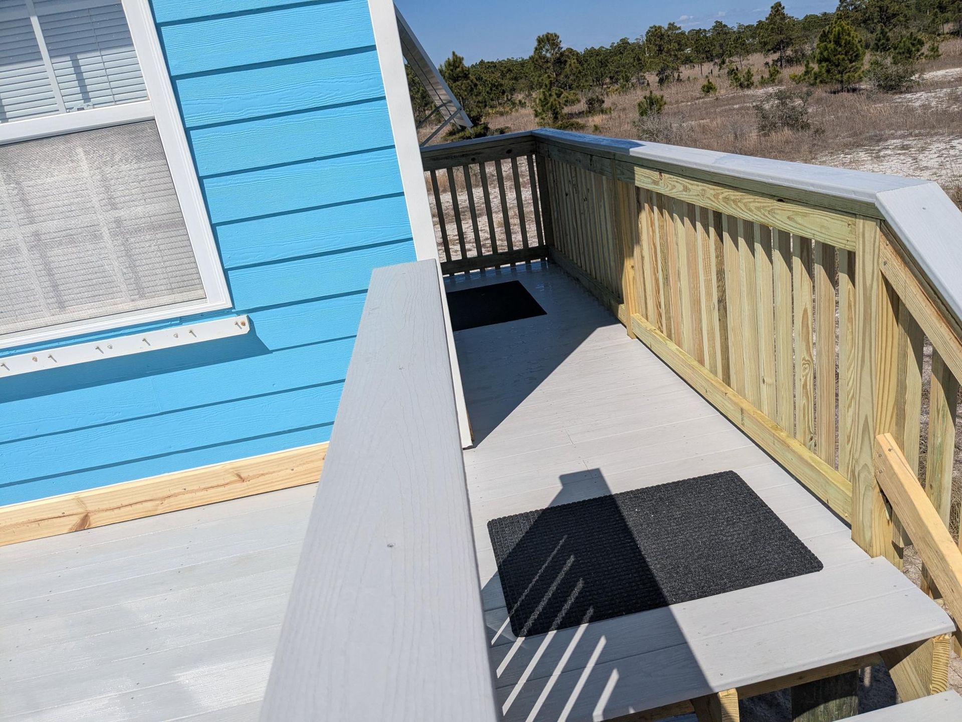 Blue building with a wooden deck, handrails, and two black mats.
