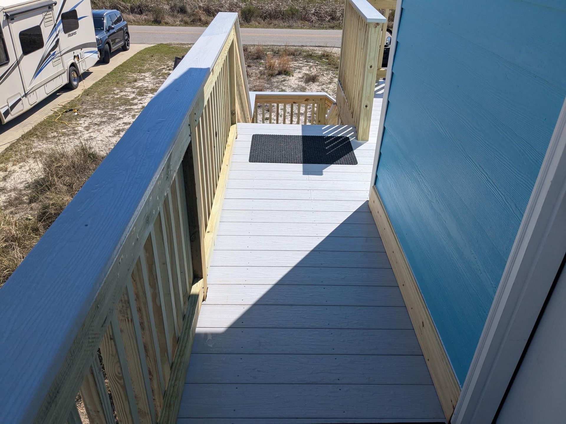 Wooden deck with railings leads to a door. RV parked nearby.