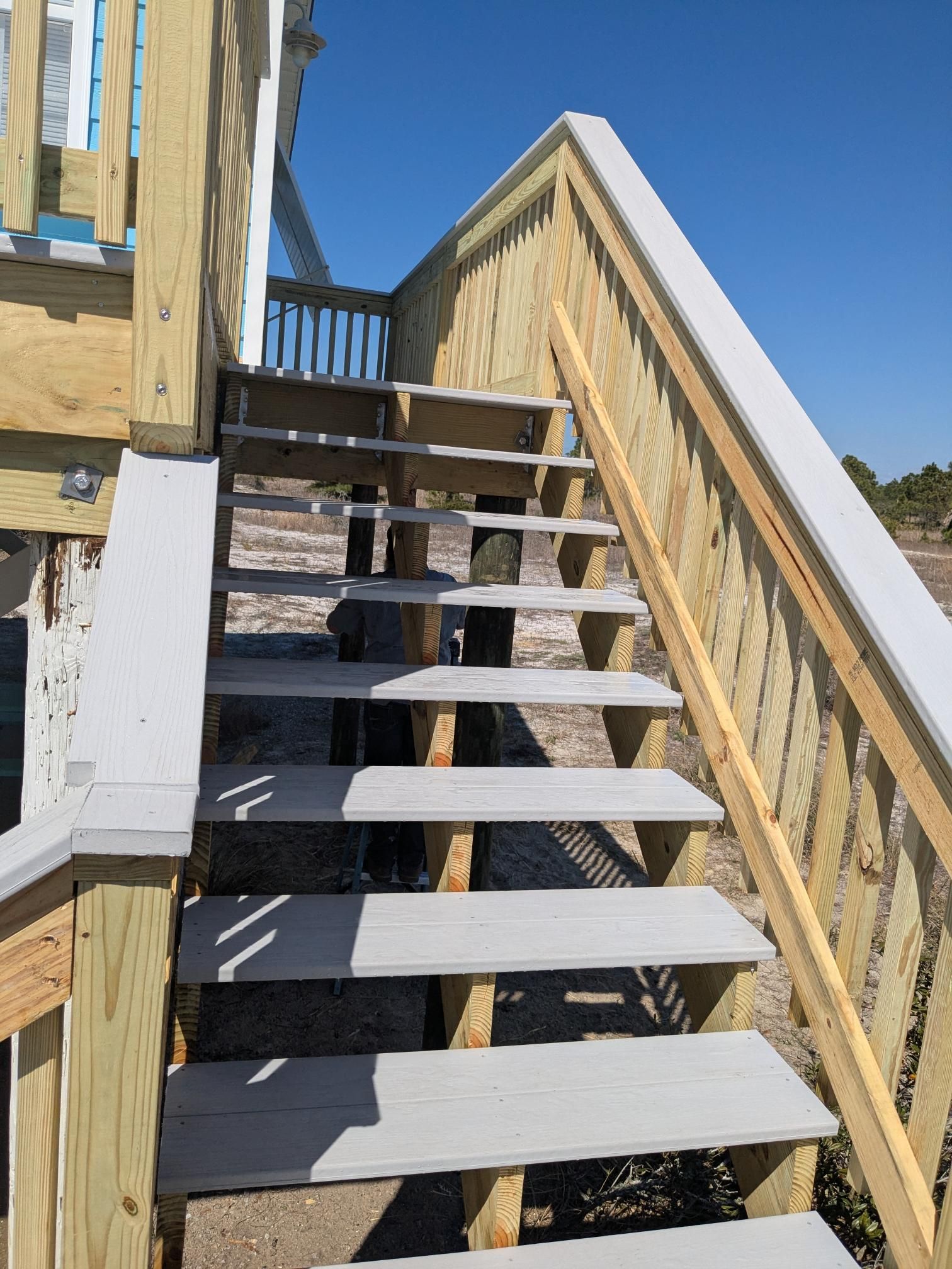 Wooden outdoor staircase leading up to a building, with gray steps and a light-colored handrail.