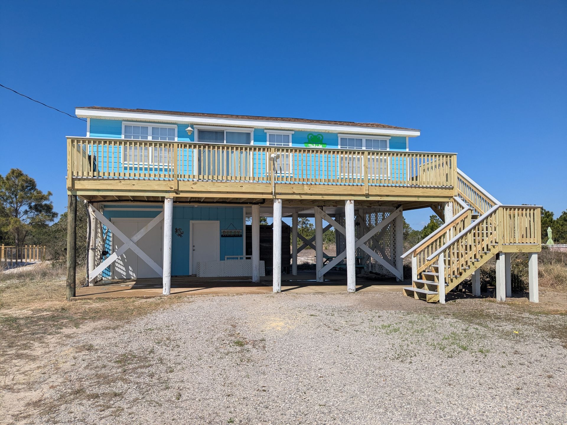 Beach house with blue siding, elevated wooden deck, and gravel driveway.