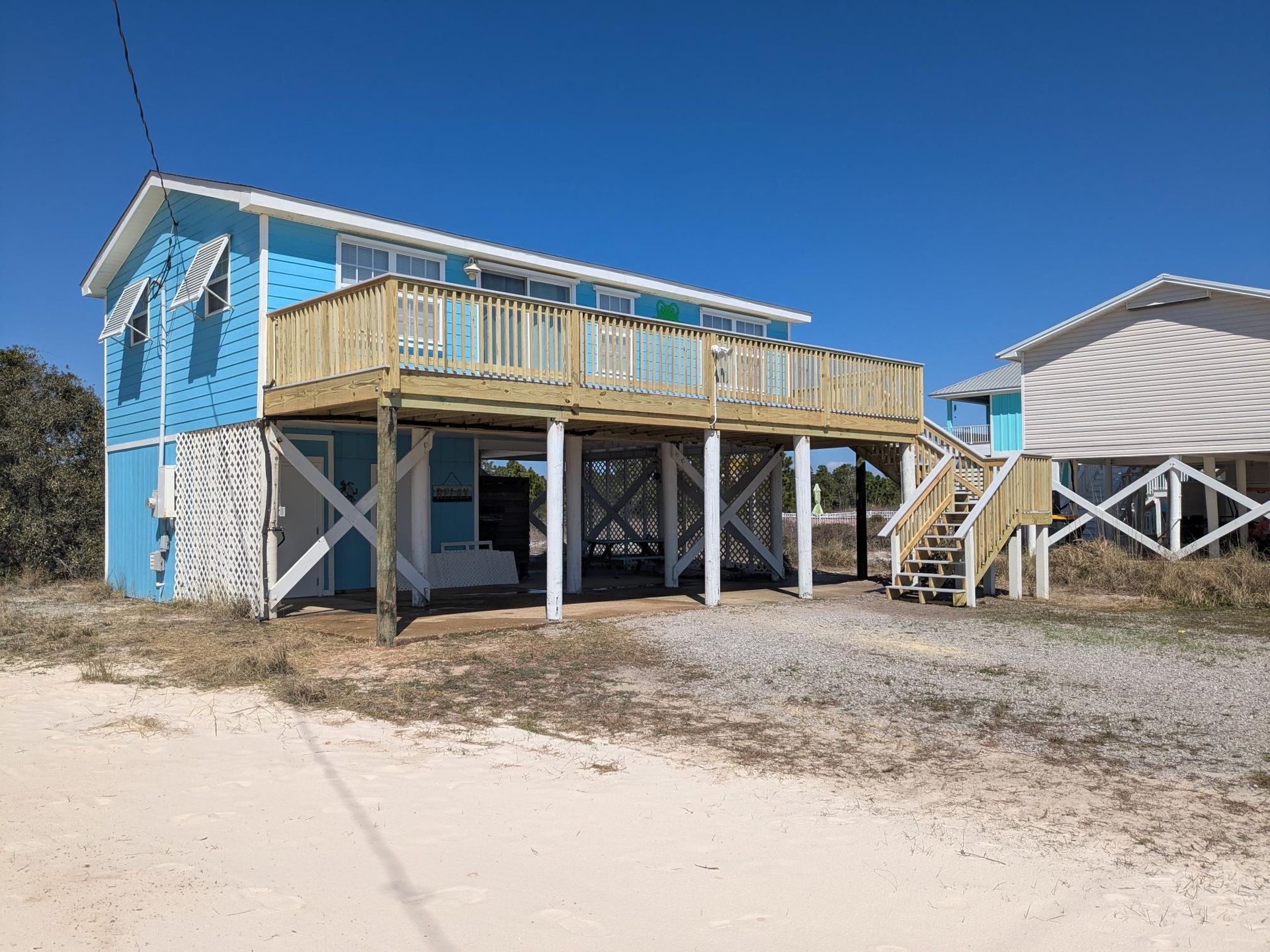 Blue beach house on stilts with wooden deck; clear blue sky.