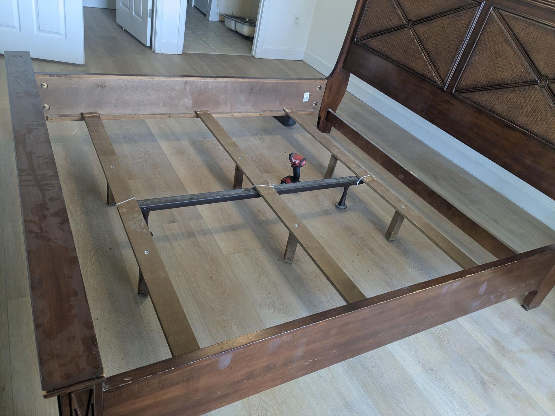 Wooden bed frame with woven headboard, partially disassembled on a wood floor.