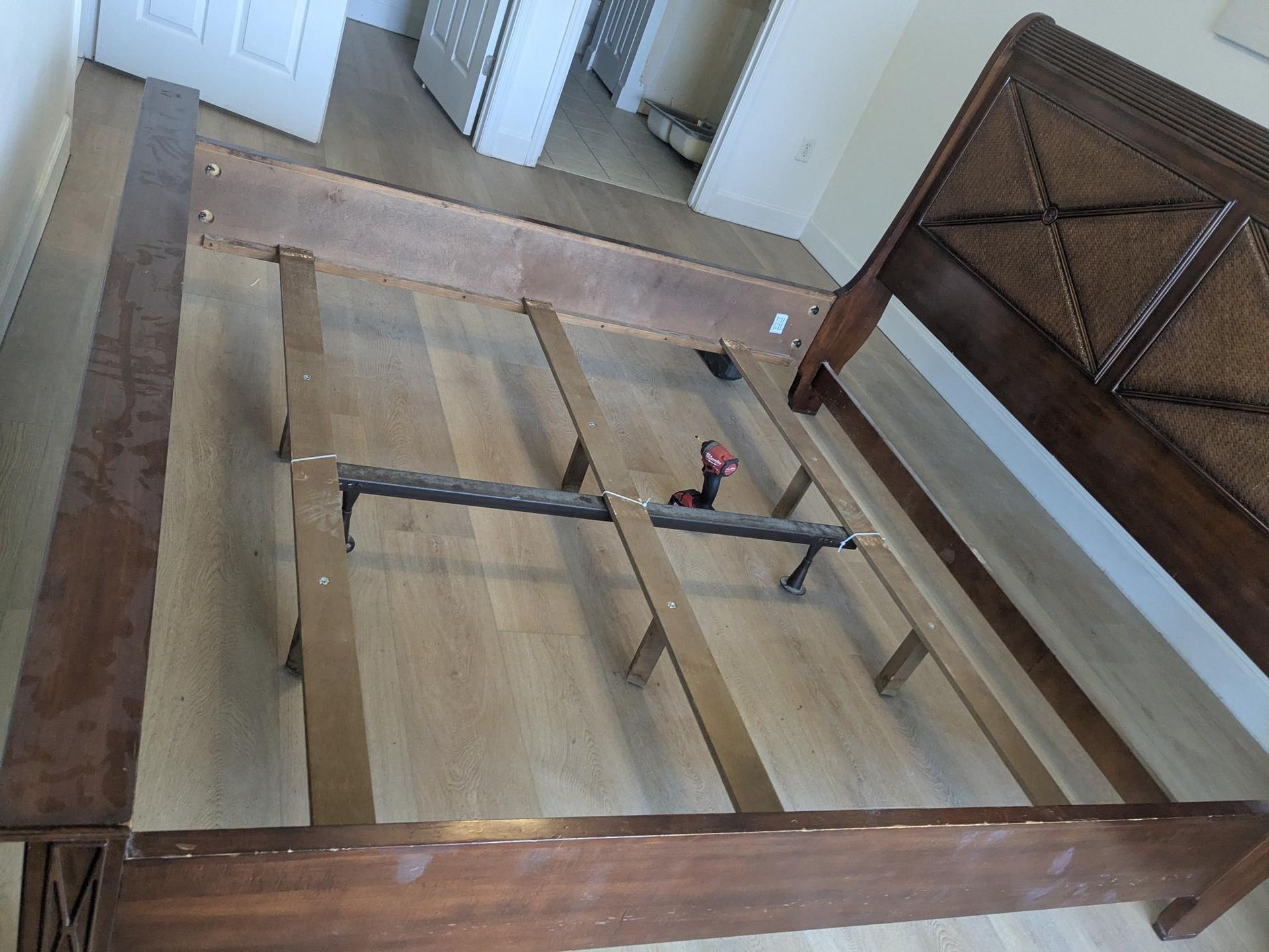 Wooden bed frame disassembled on hardwood floor, headboard with woven detail in the upper right.