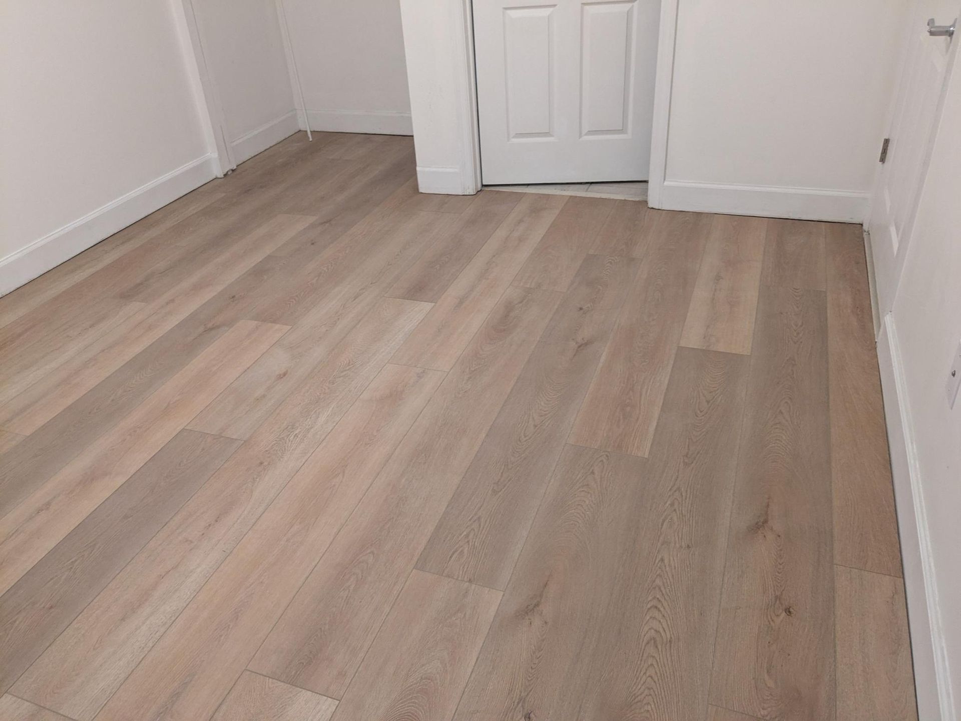 Light-colored wood-look flooring installed in a room with white walls and a closed white door.