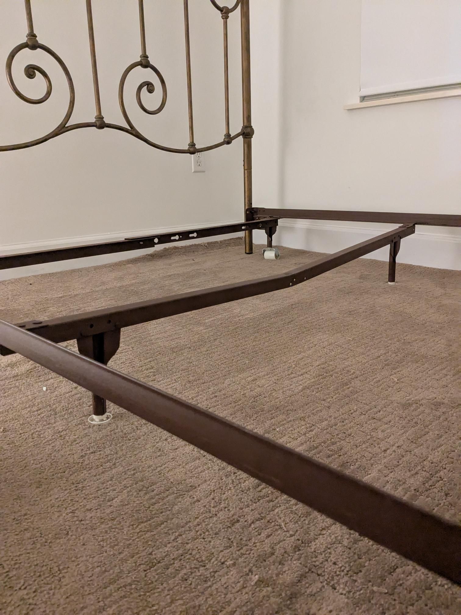 Metal bed frame with decorative headboard on a carpeted floor.