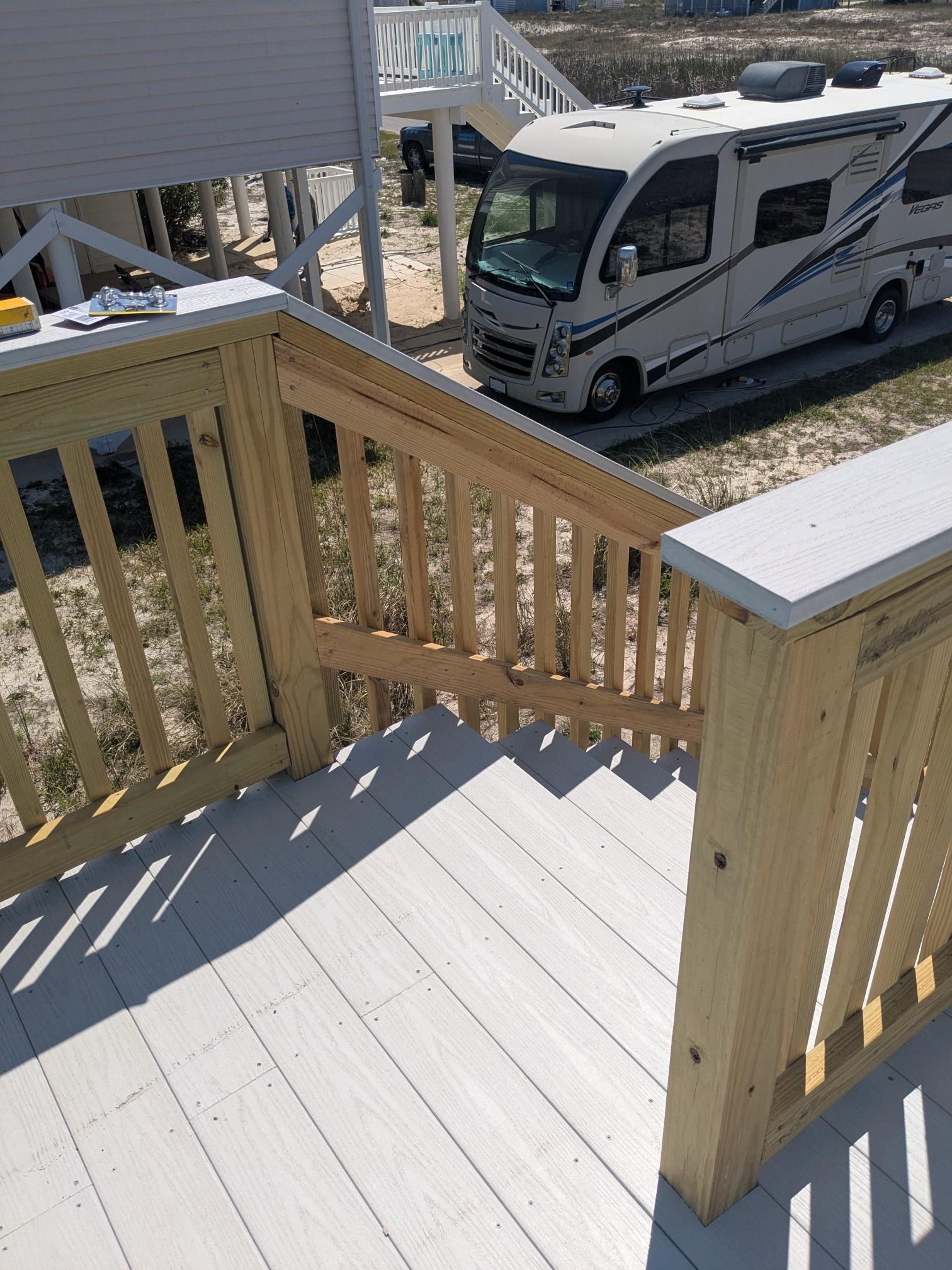 Wooden deck with stairs, light wood railing, white painted deck boards, and an RV parked nearby.