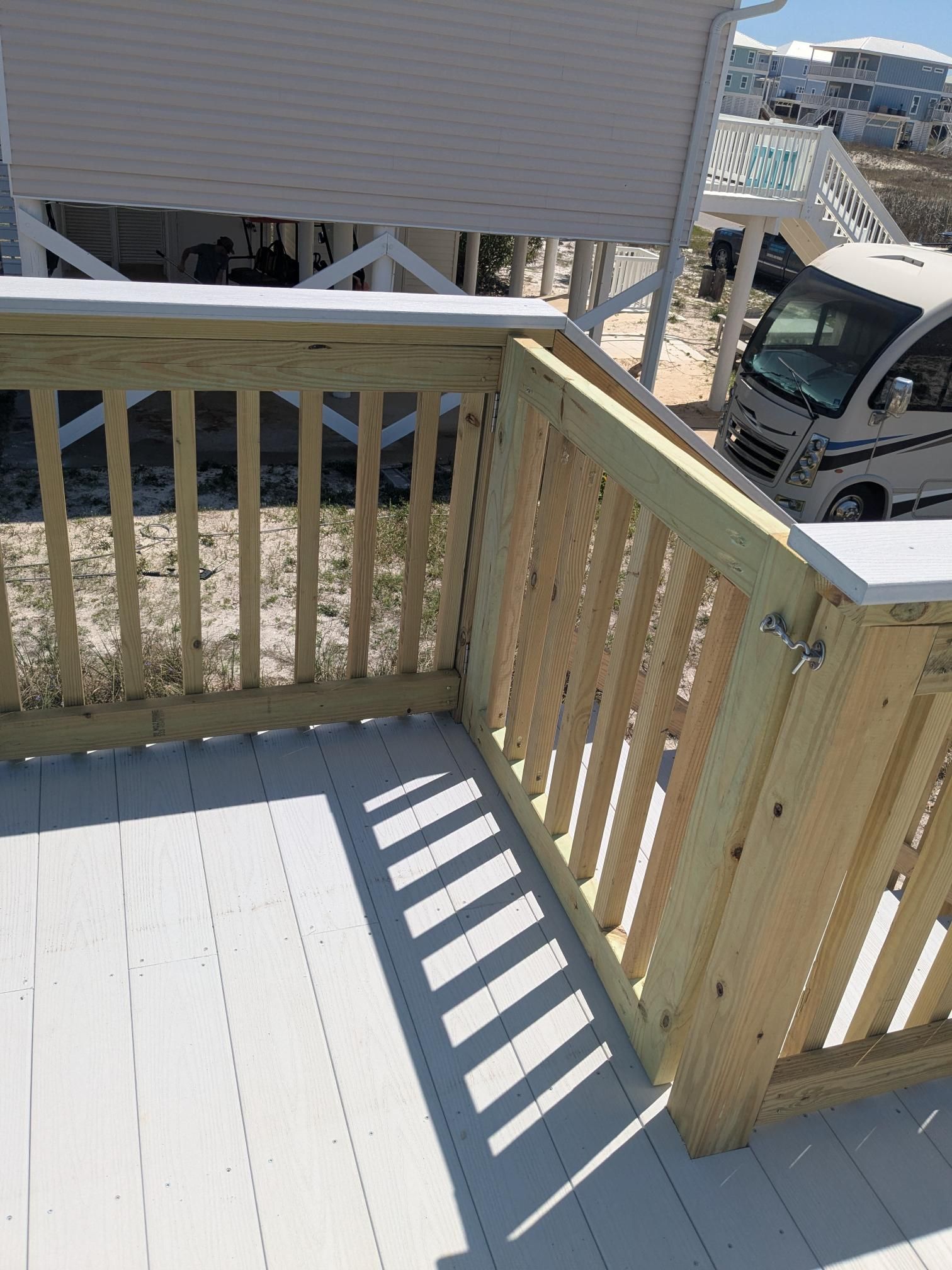 Wooden deck with white railing, partially open gate, and shadow.