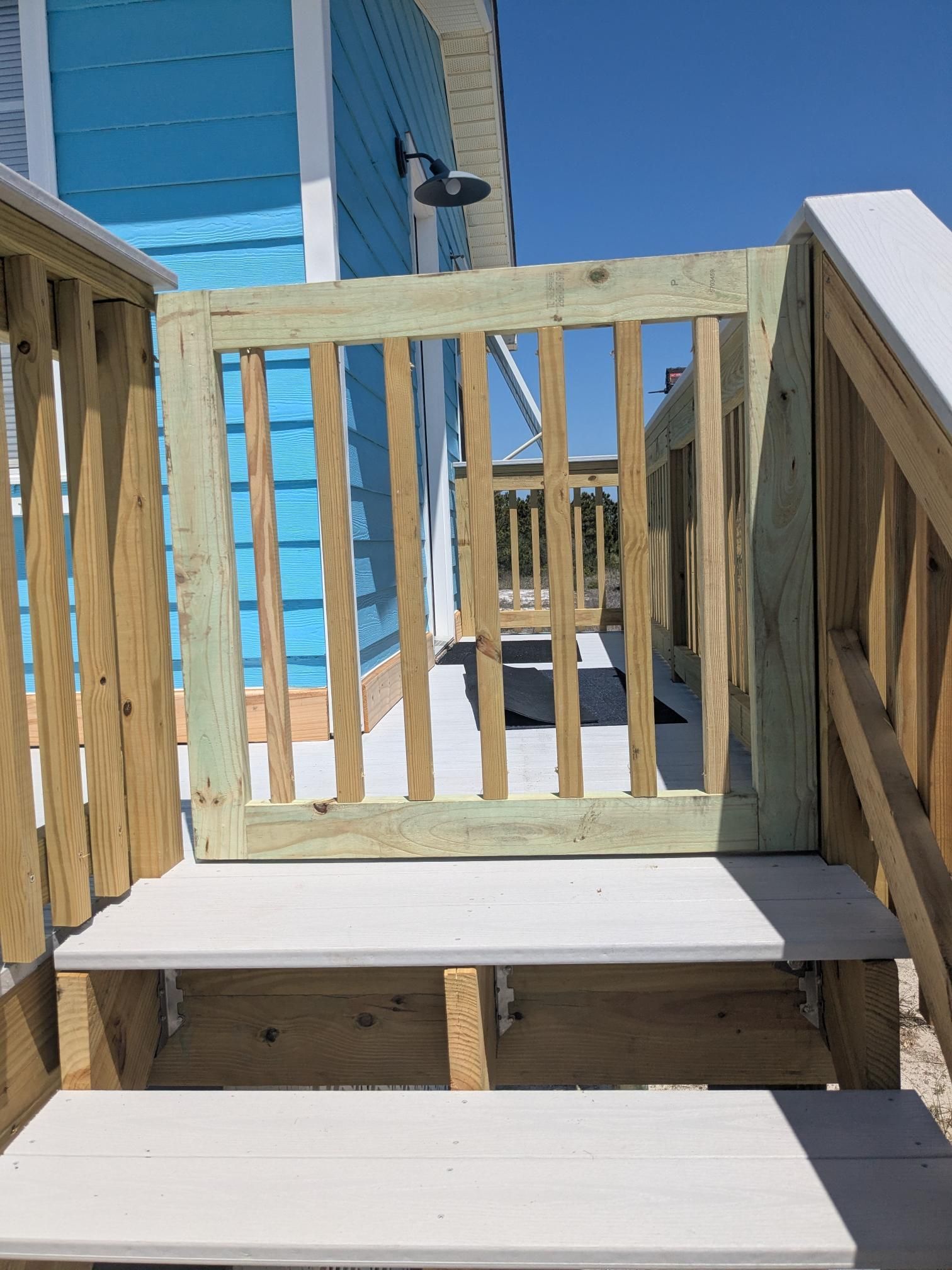 Wooden gate on a deck with steps, painted in shades of green and brown, under a blue sky.