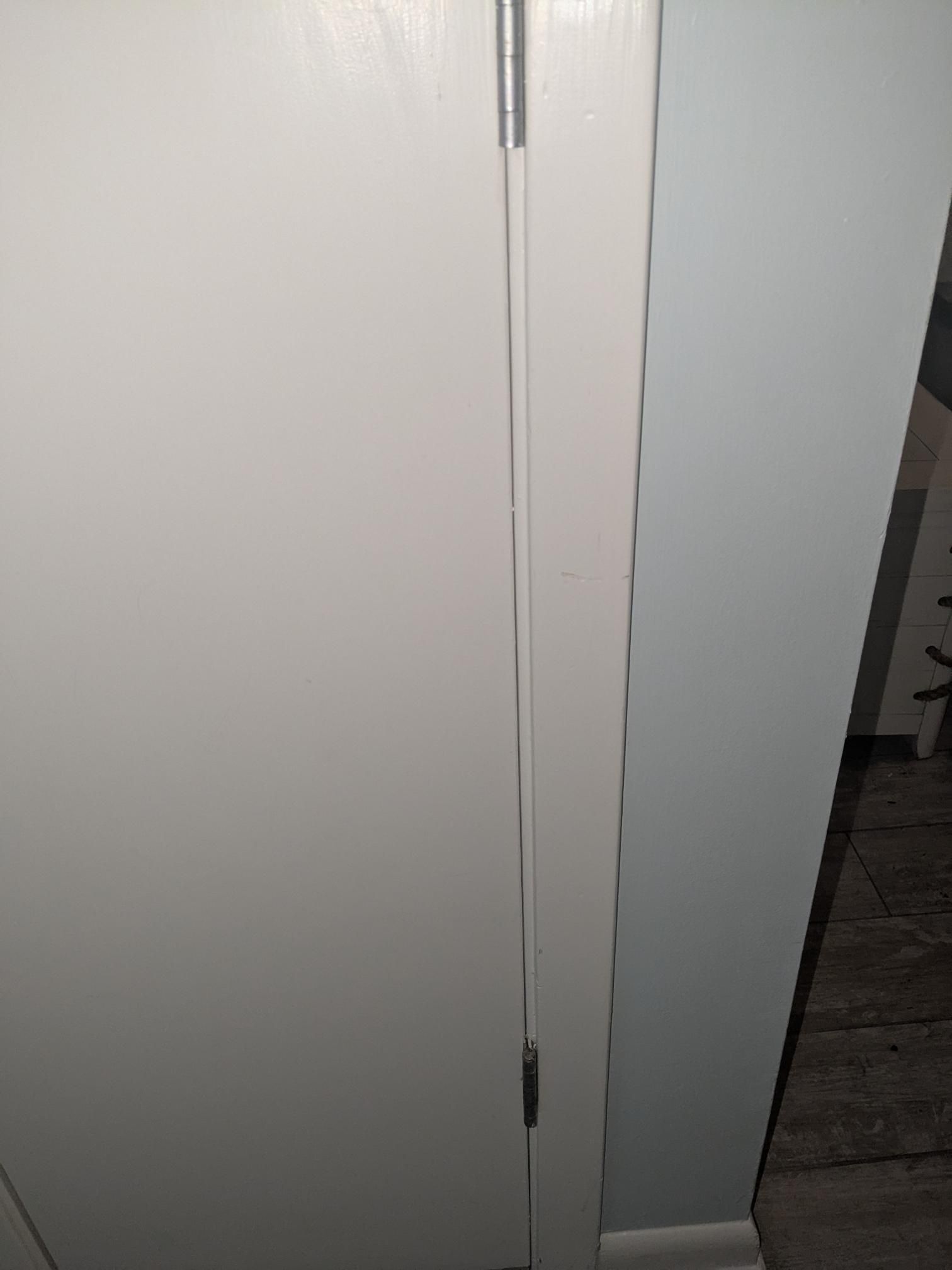 White door slightly ajar against a light blue wall. A silver hinge is visible.