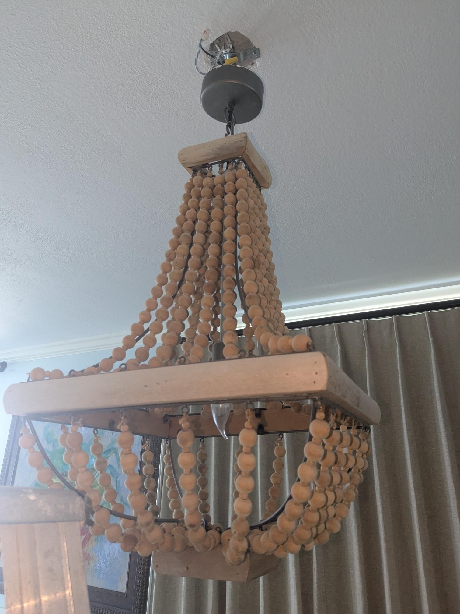Wooden beaded chandelier hanging from a white ceiling with exposed wiring.