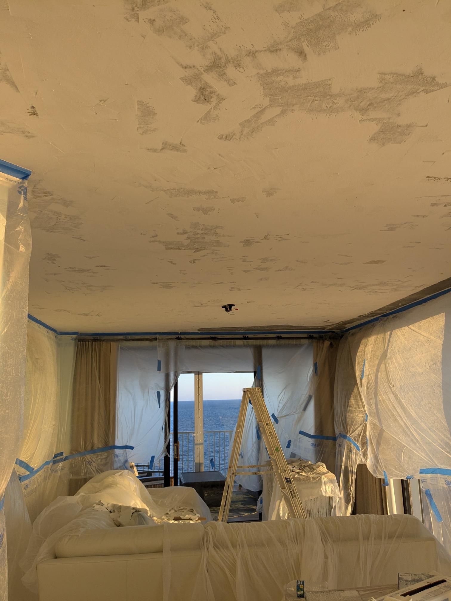 Room under renovation with plastic sheeting, tape, and a view of the ocean.