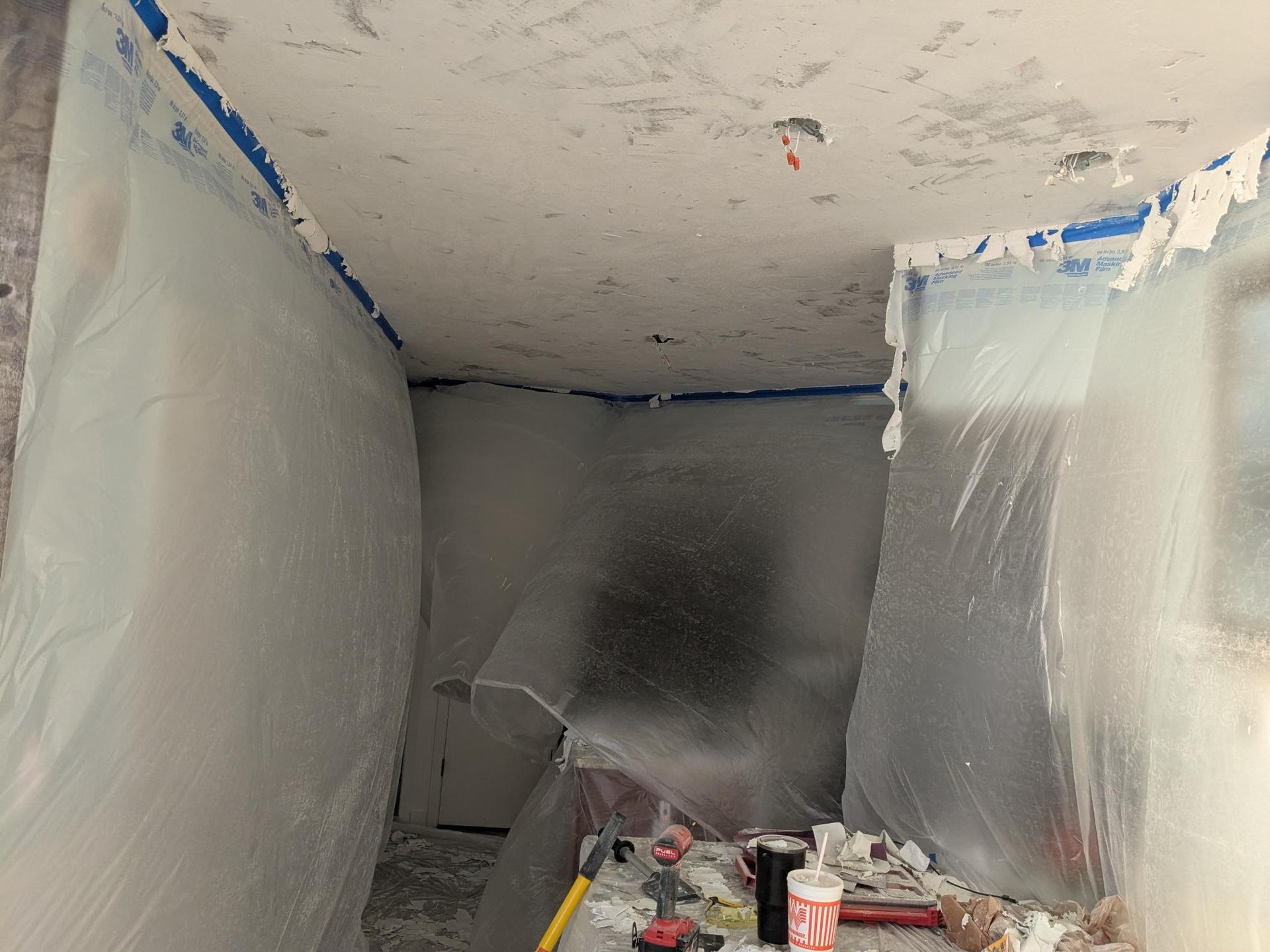 Room under construction, plastic sheeting covering walls. Ceiling and walls show signs of previous work.