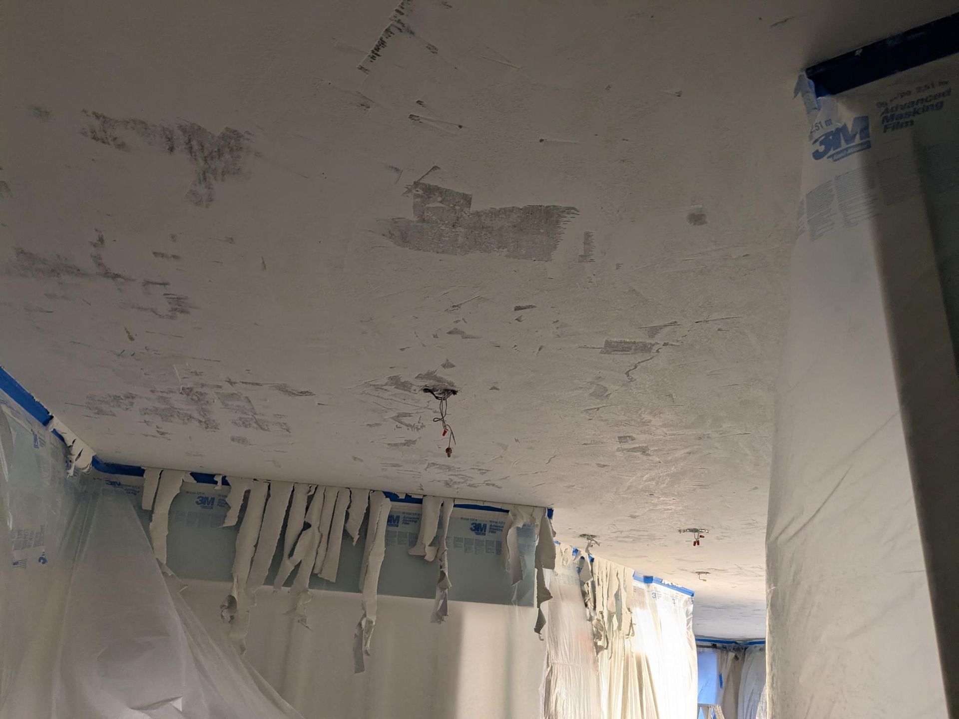 Ceiling with peeling paint during renovation, covered in plastic sheeting and tape.