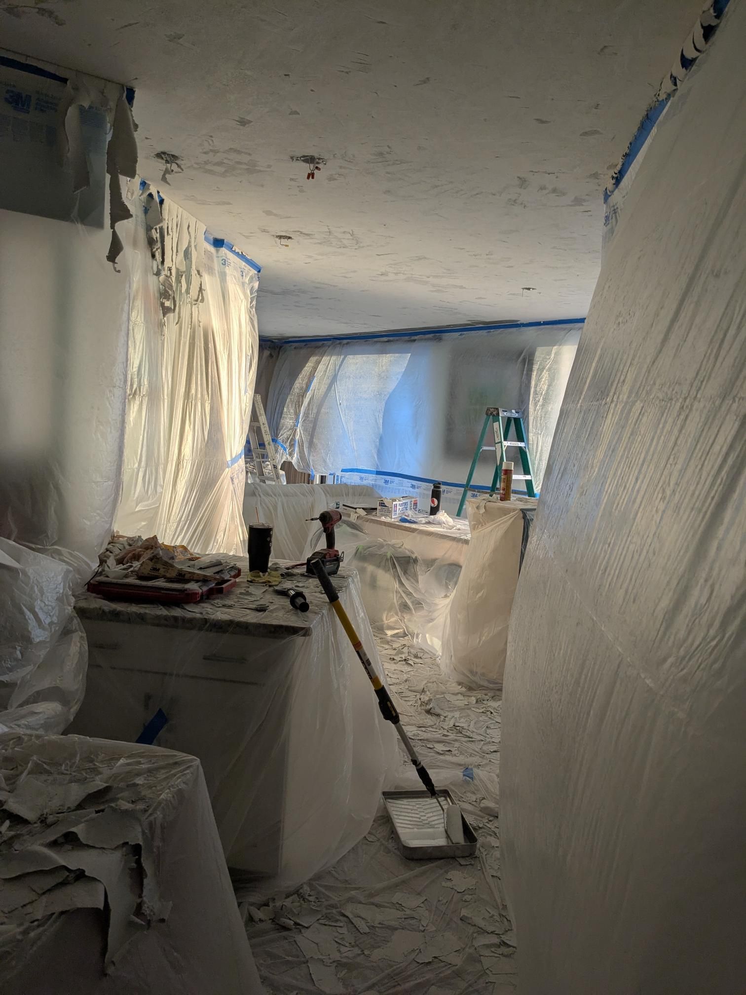 Room under renovation, covered in plastic sheeting. Construction tools and debris visible.