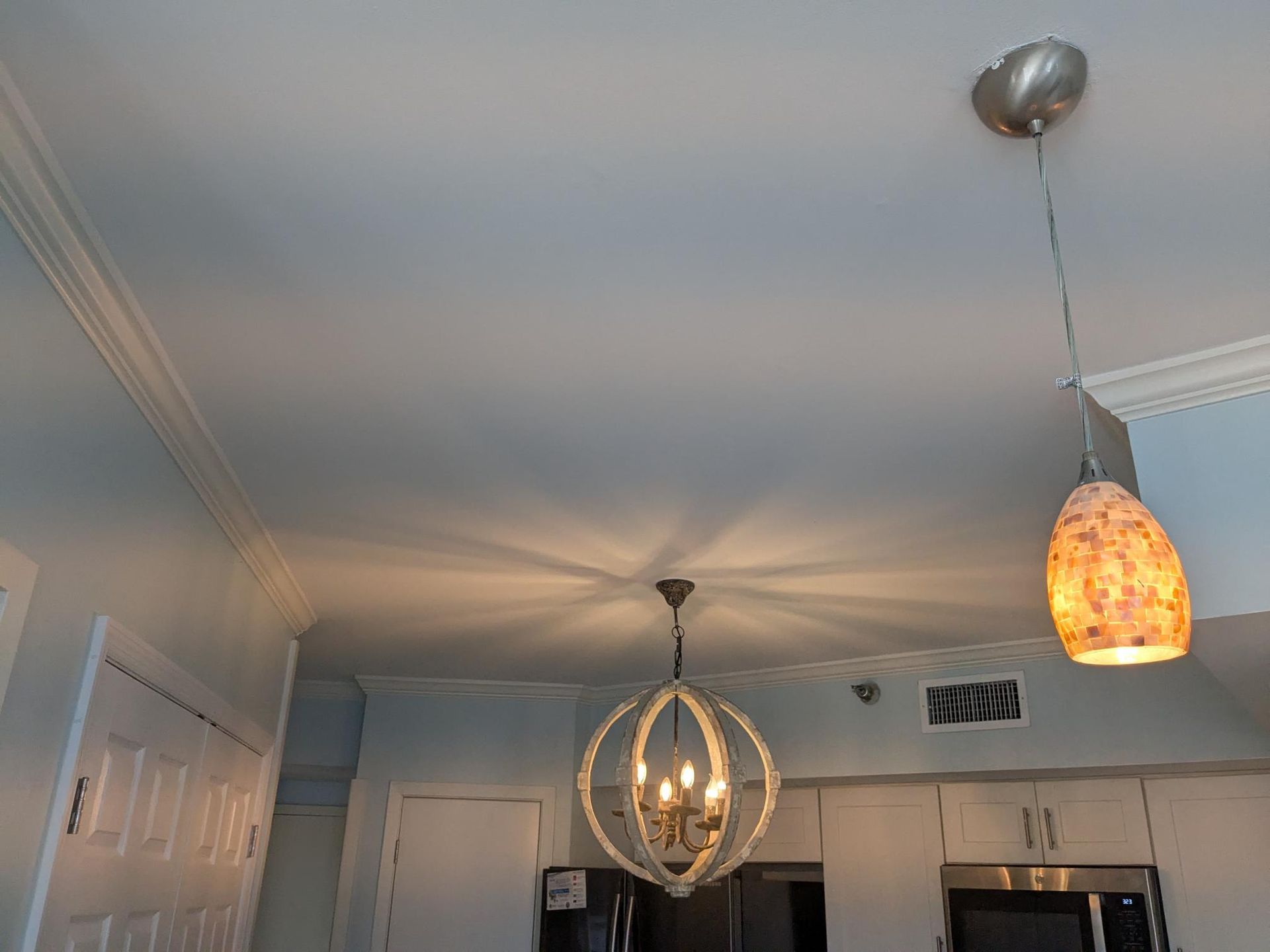 Ceiling with two pendant lights and a spherical chandelier over a kitchen area.